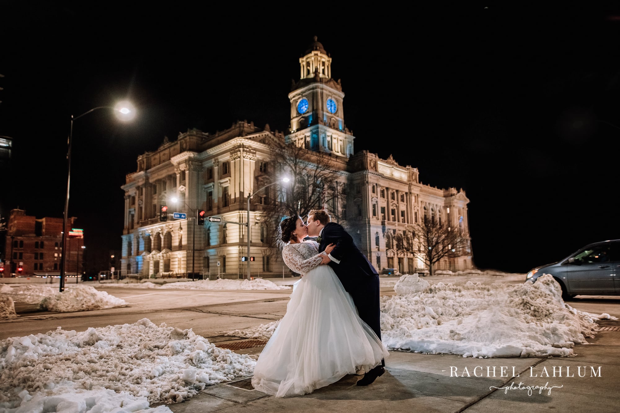 Groom dips and kisses bride in front of blue-lit Polk County Courthouse in Des Moines, Iowa.