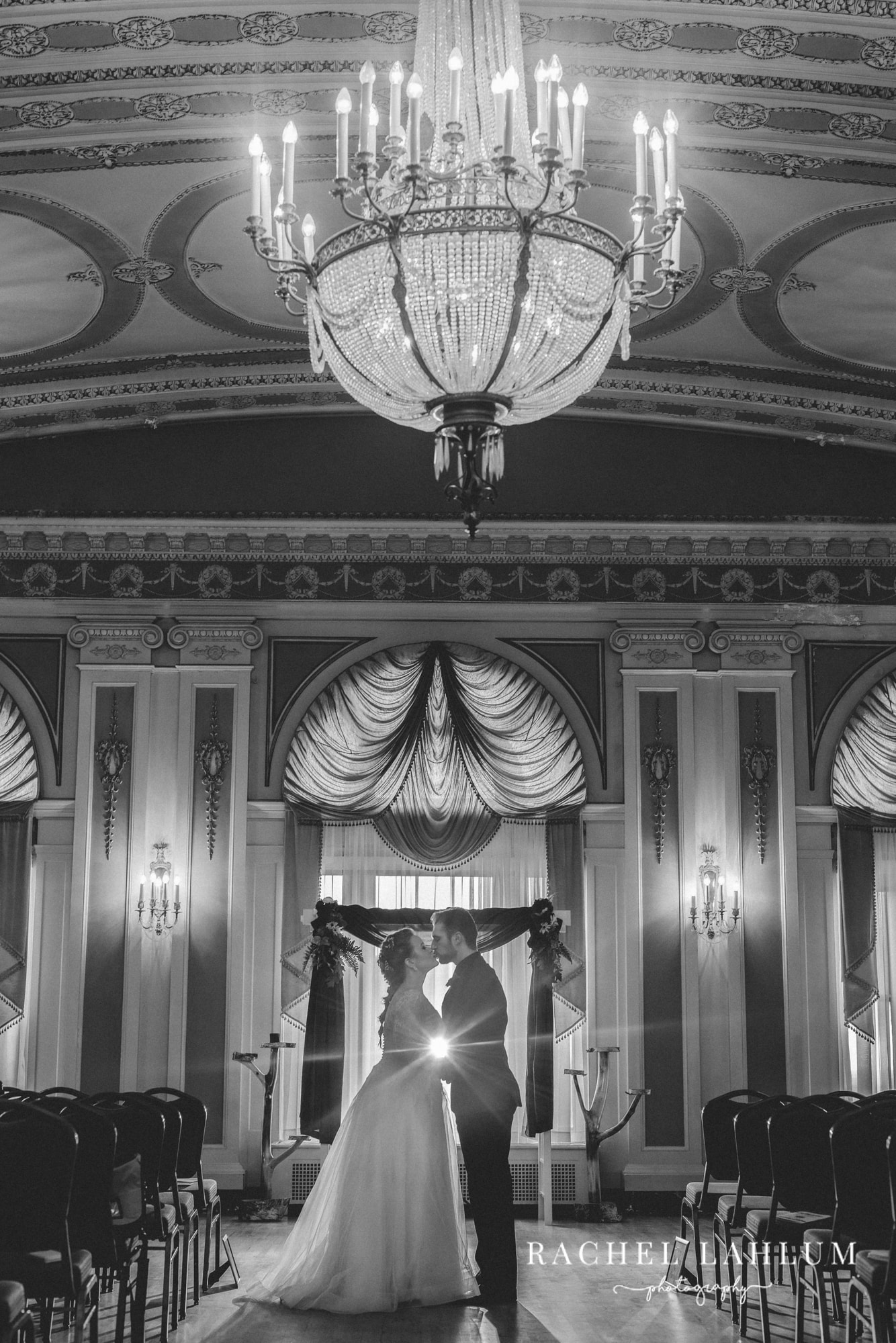 Black and white photo of newly wed couple kissing under a chandelier in the ceremony space at Greysolon. 