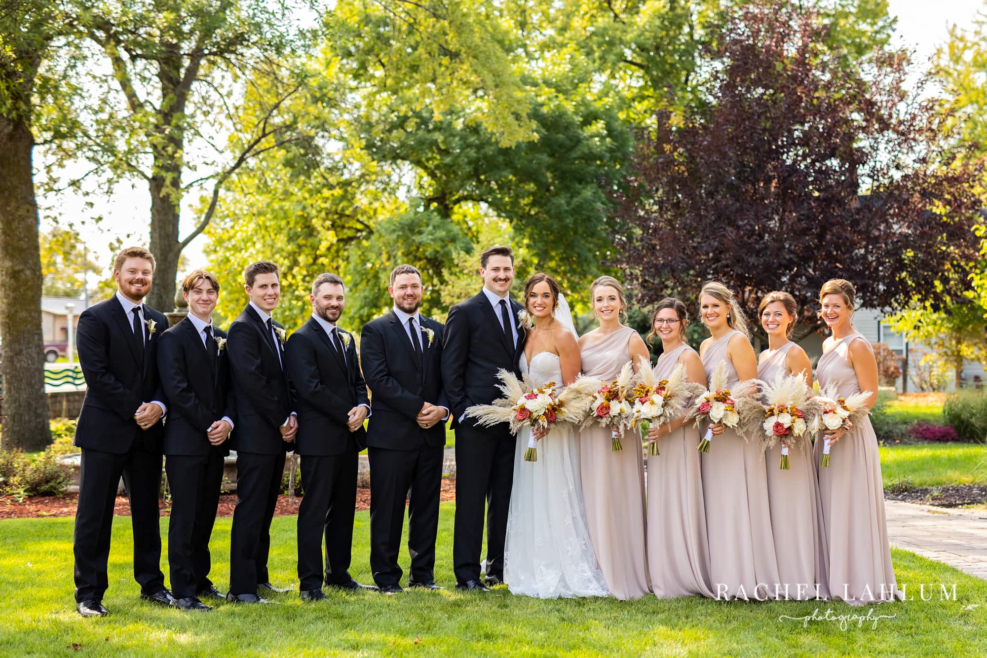A wedding party poses in a line for a wedding photo at Legacy of the Lakes Museum.