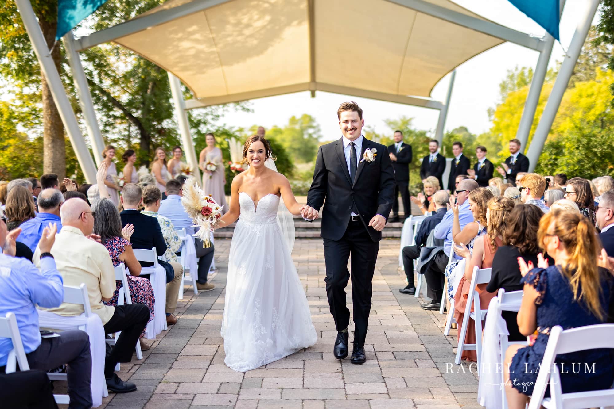 Newly-married bride and groom smile while holding hands and walking down the aisle at Legacy of the Lakes Museum in Alexandria, Minnesota.