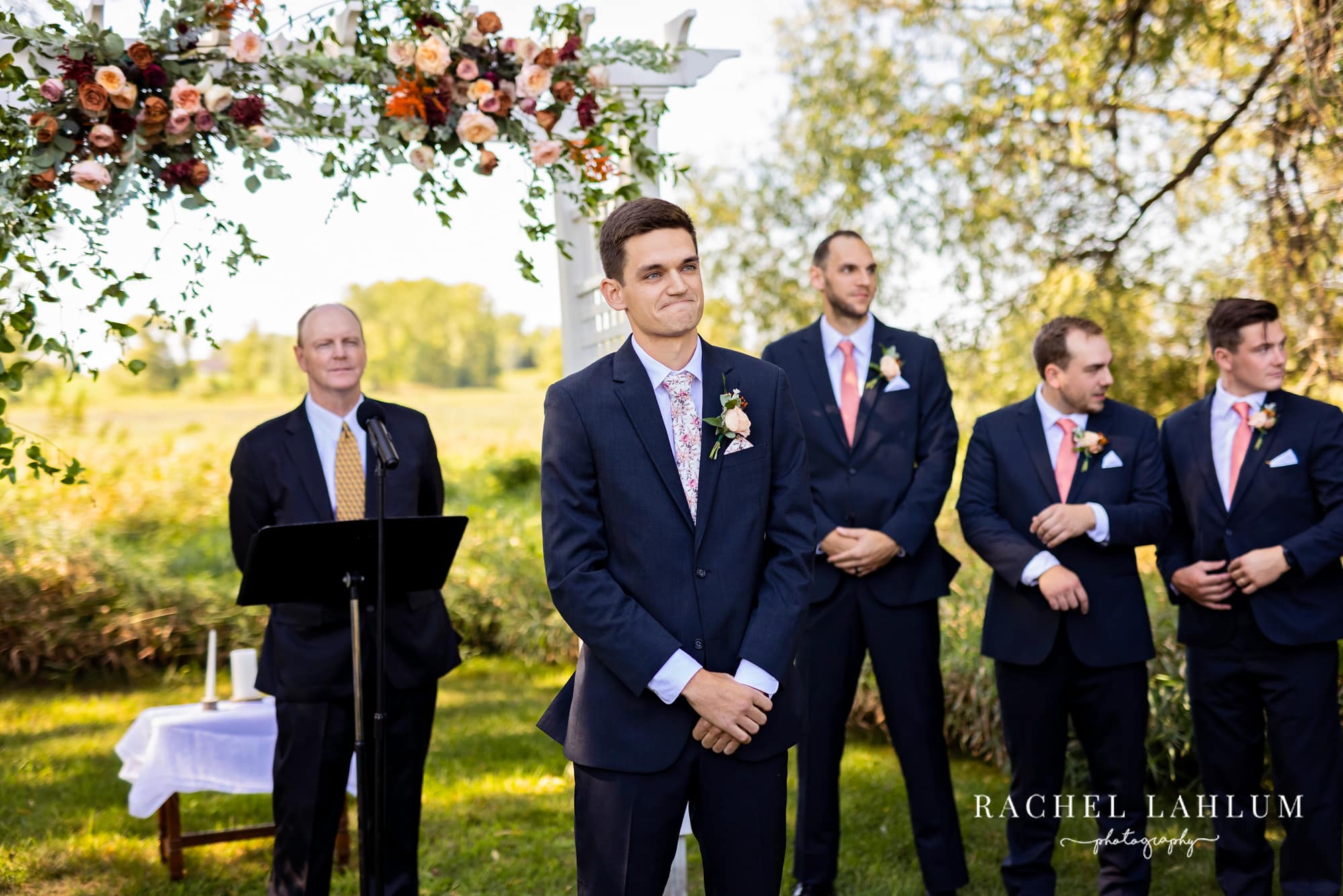 Groom watches bride walk down the aisle during outdoor wedding ceremony at the Cottage Farmhouse in Glencoe, Minnesota.