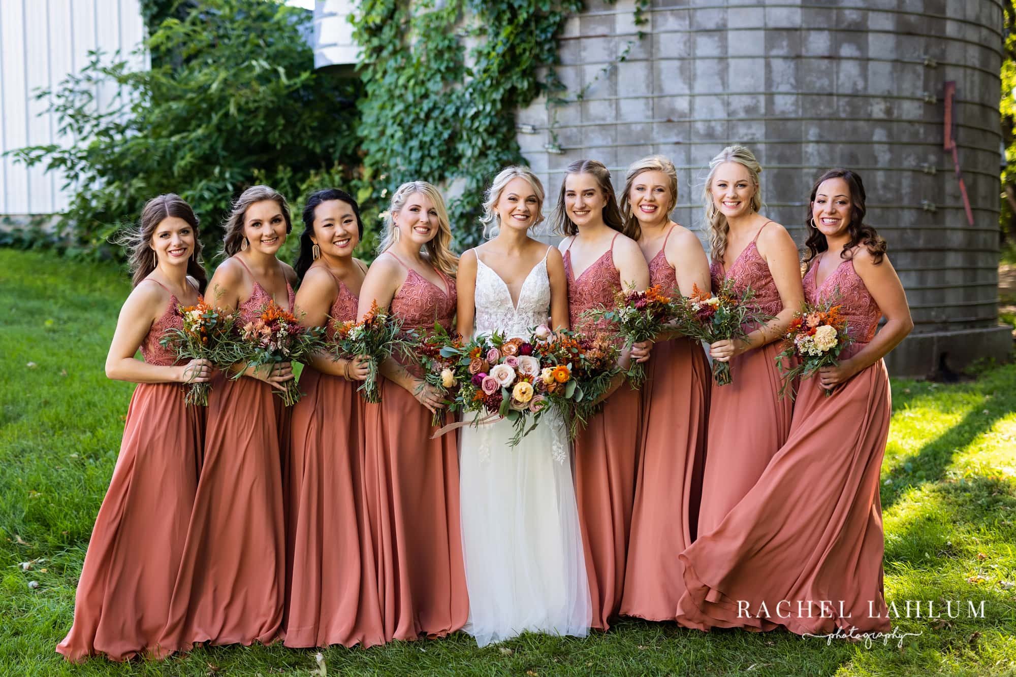 Bride and bridesmaids pose with bouquets in front of the silo at The Cottage Farmhouse.