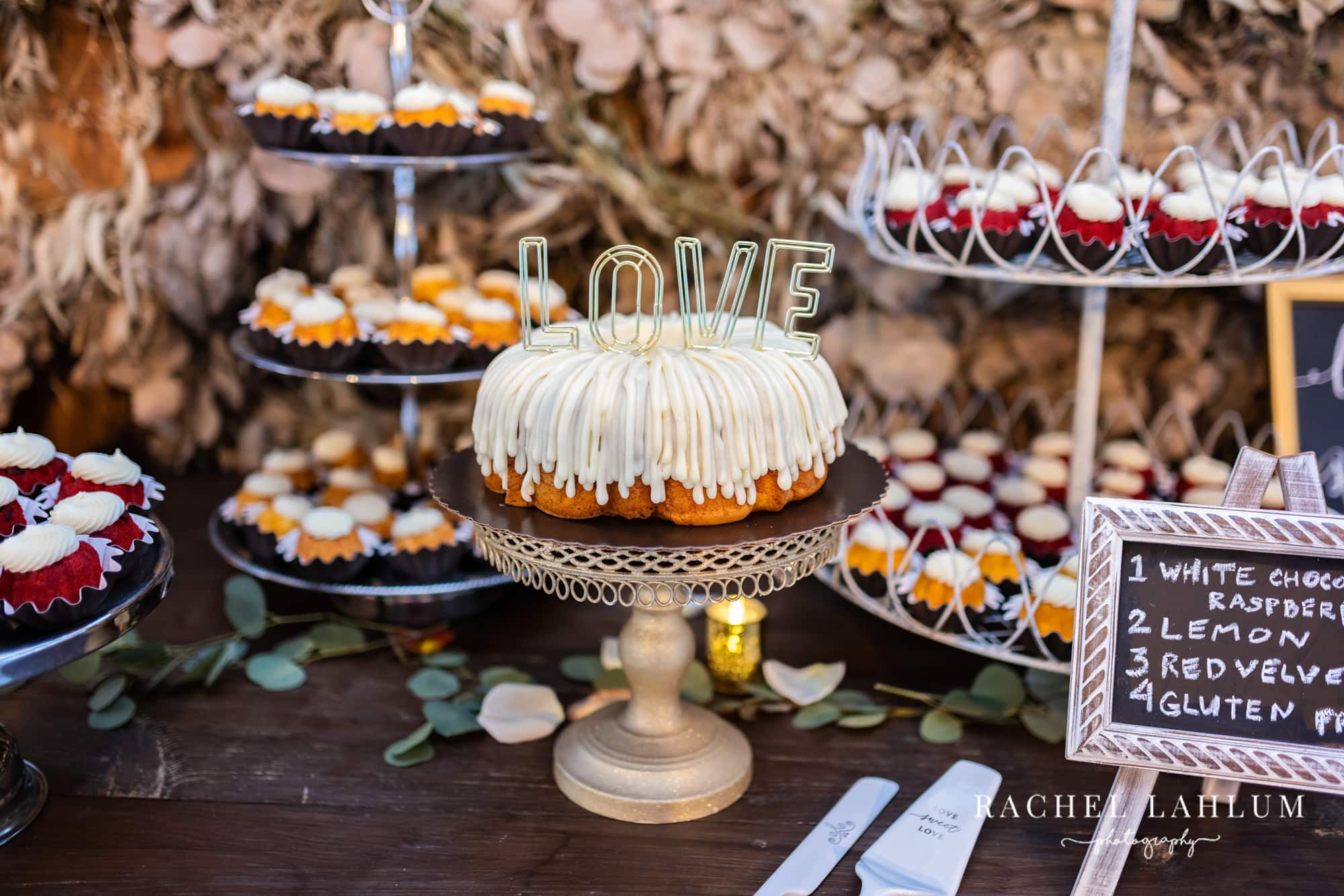 A cake with letters spelling “love” on top sits in the center of the dessert table.