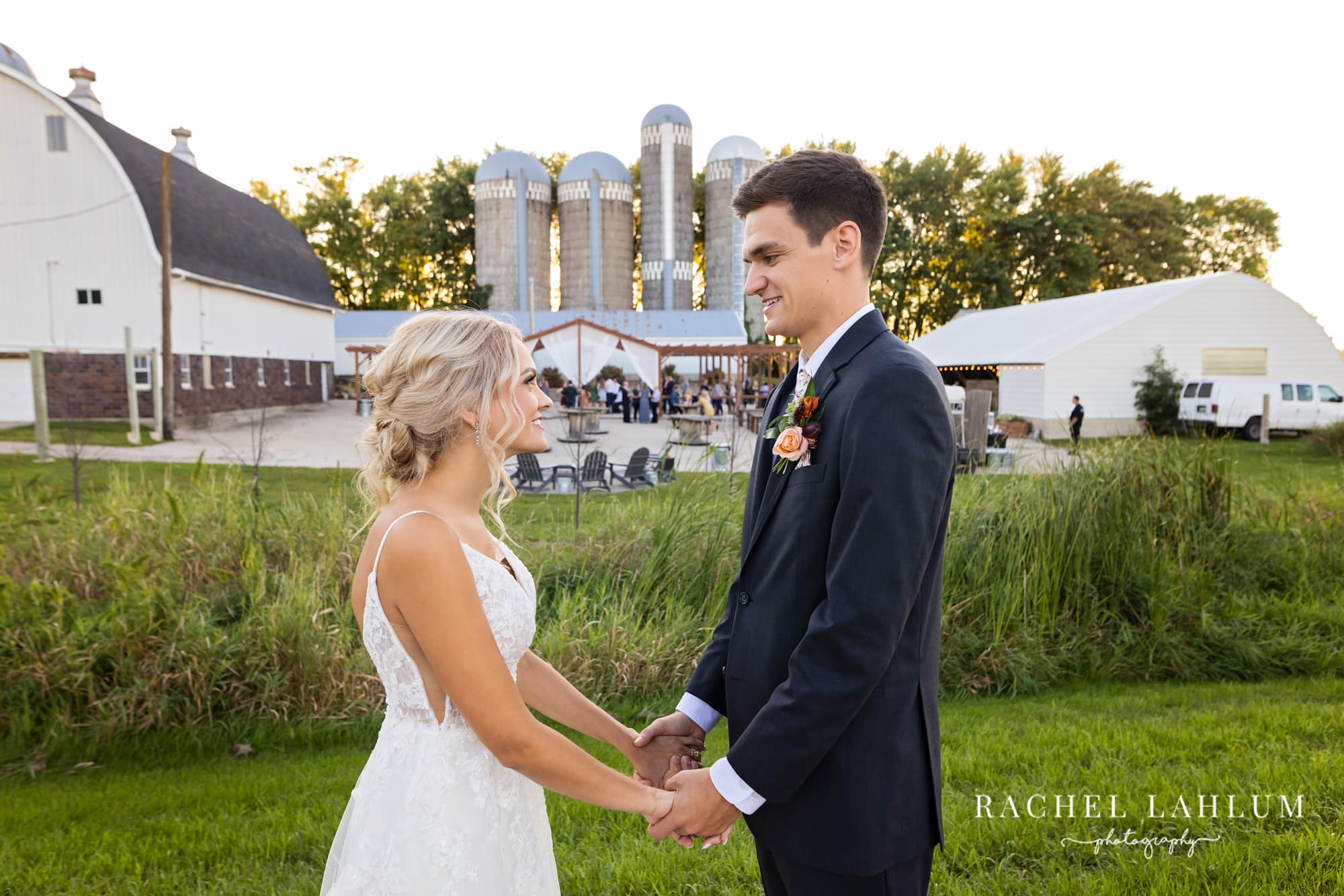 Bride and groom hold hands and look at each other in front of the silos of the Cottage Farmhouse.