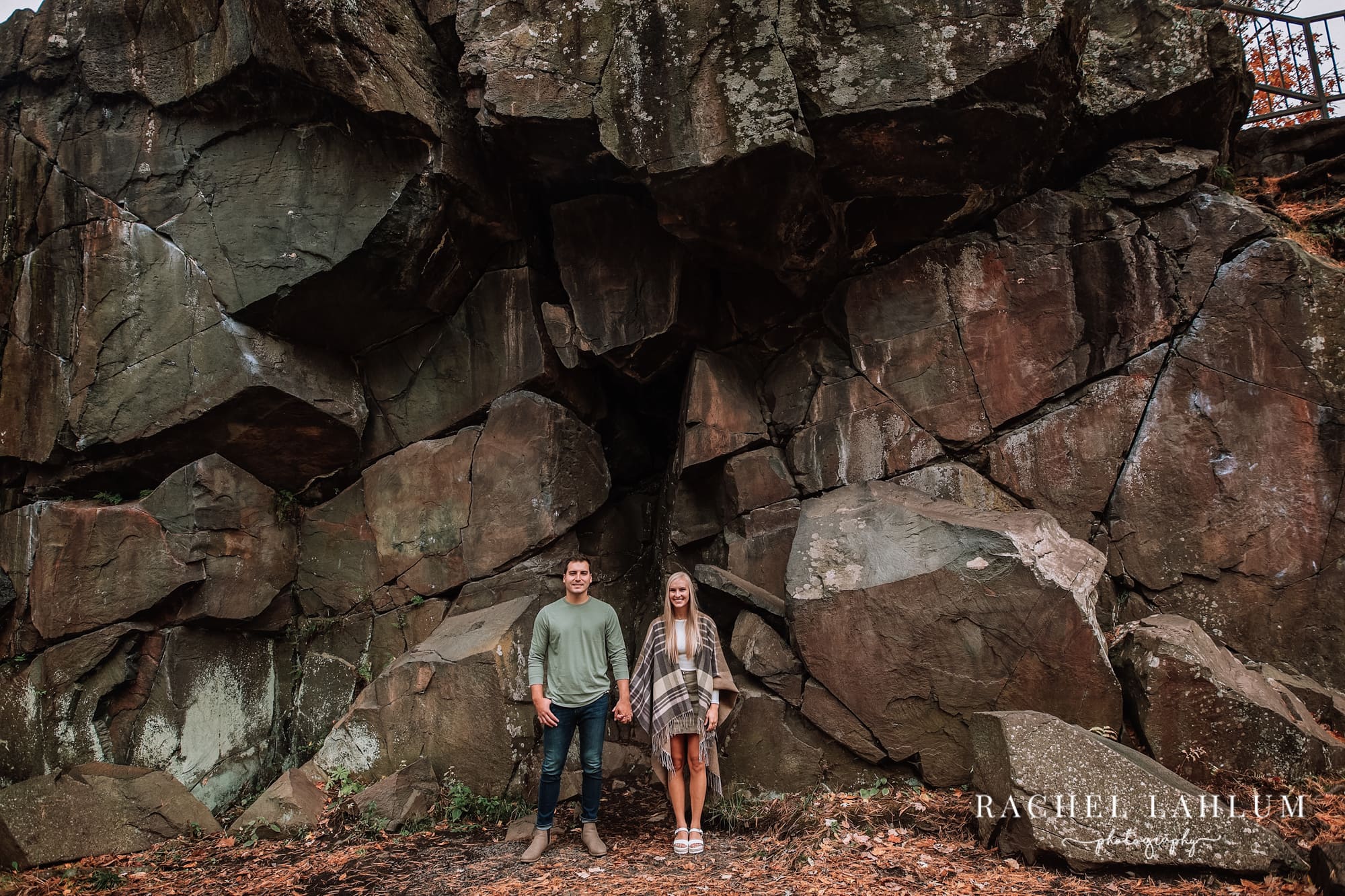 Engaged couple hold hands in front of rock feature in Taylors Falls, Minnesota. 