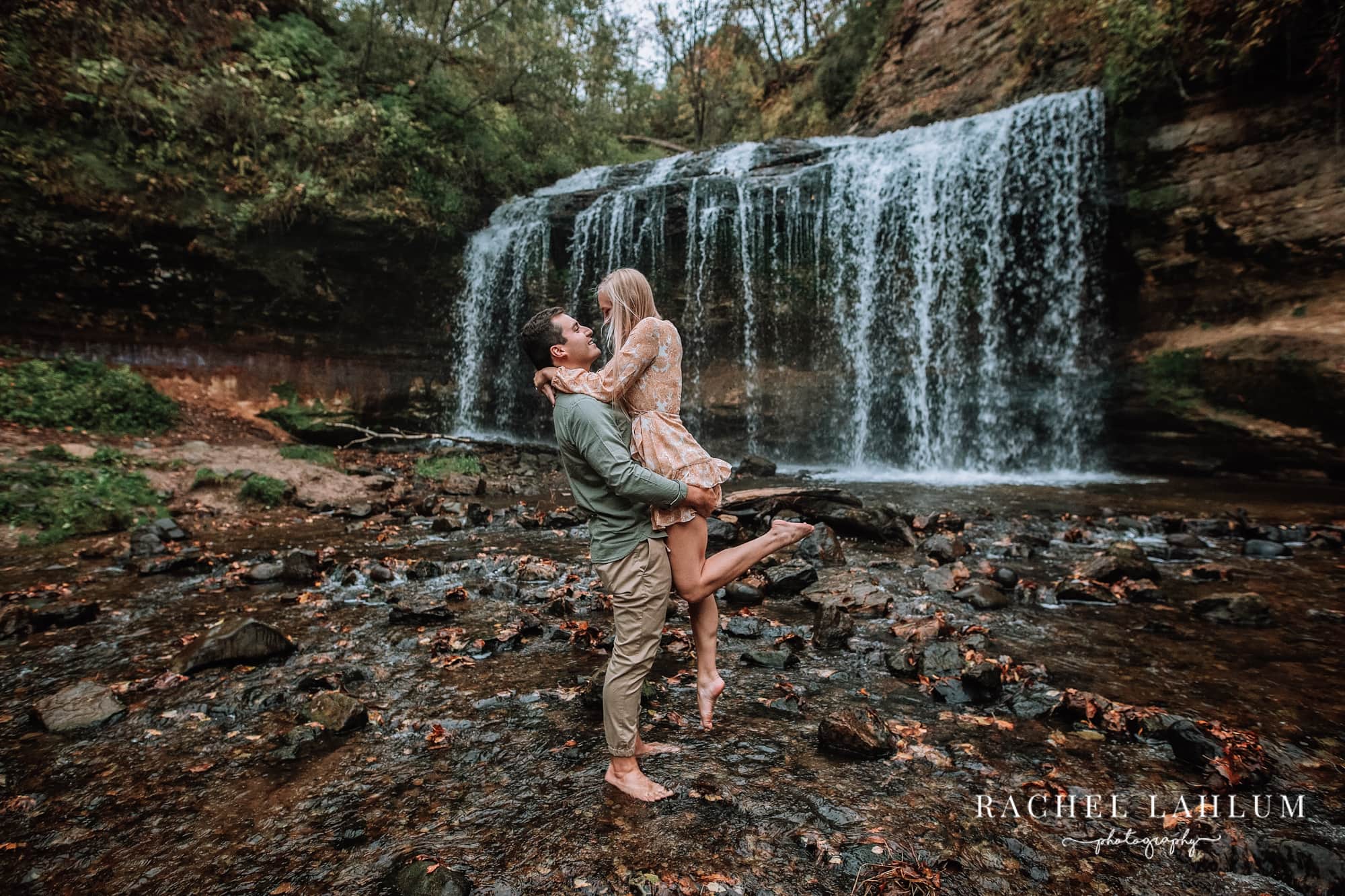 Man lifts up woman in front of waterfall at Cascade Falls in Osceola, WI.