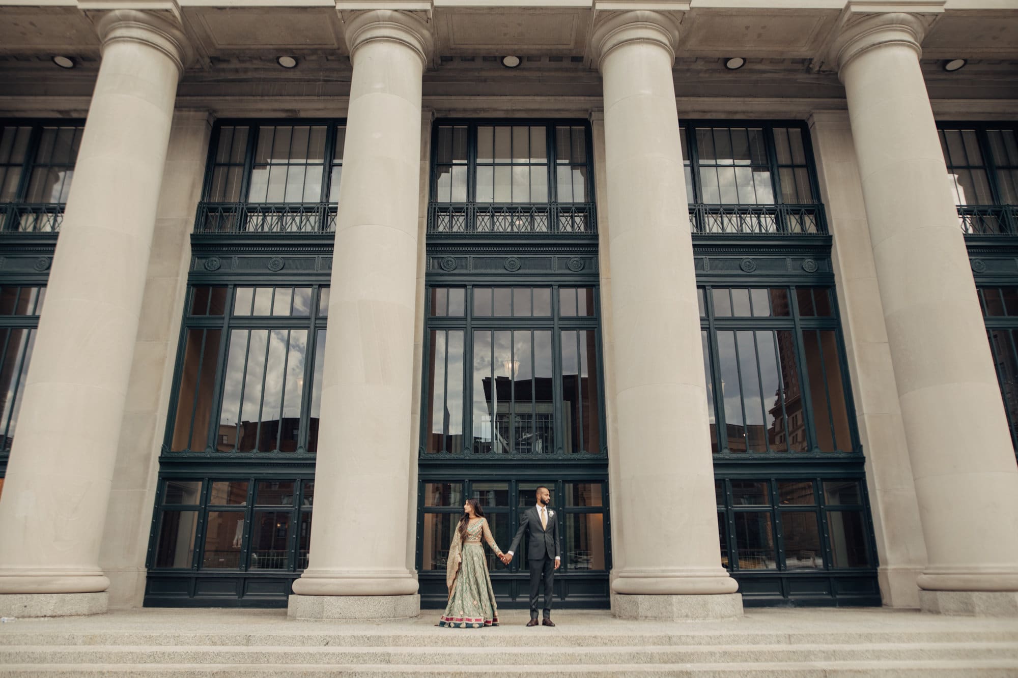 Couple stands between large stone columns holding hands at Saint Paul Union Depot.
