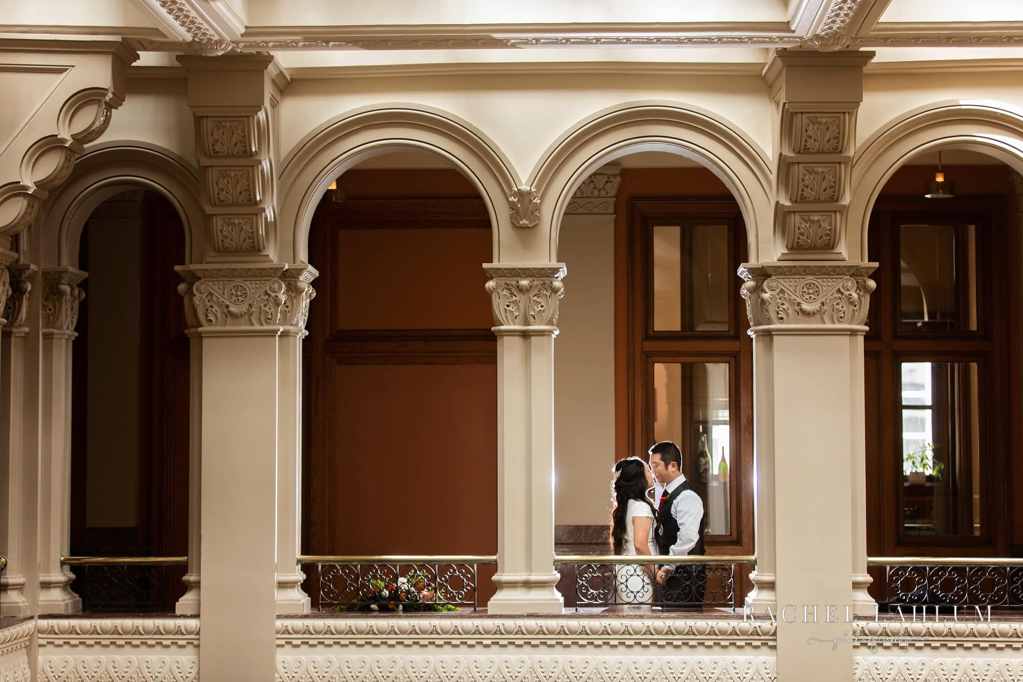 Bride and groom pose for a portrait in archway on balcony inside the Landmark Center. 