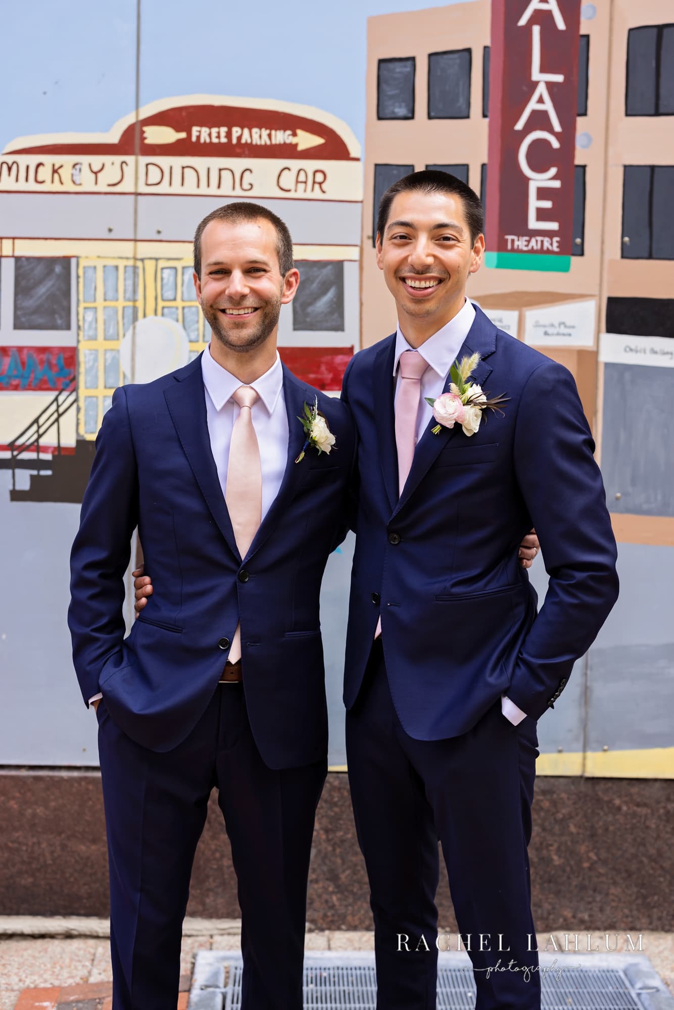 Groom and Best Man pose by mural at Seventh Place Plaza in St. Paul, MN.