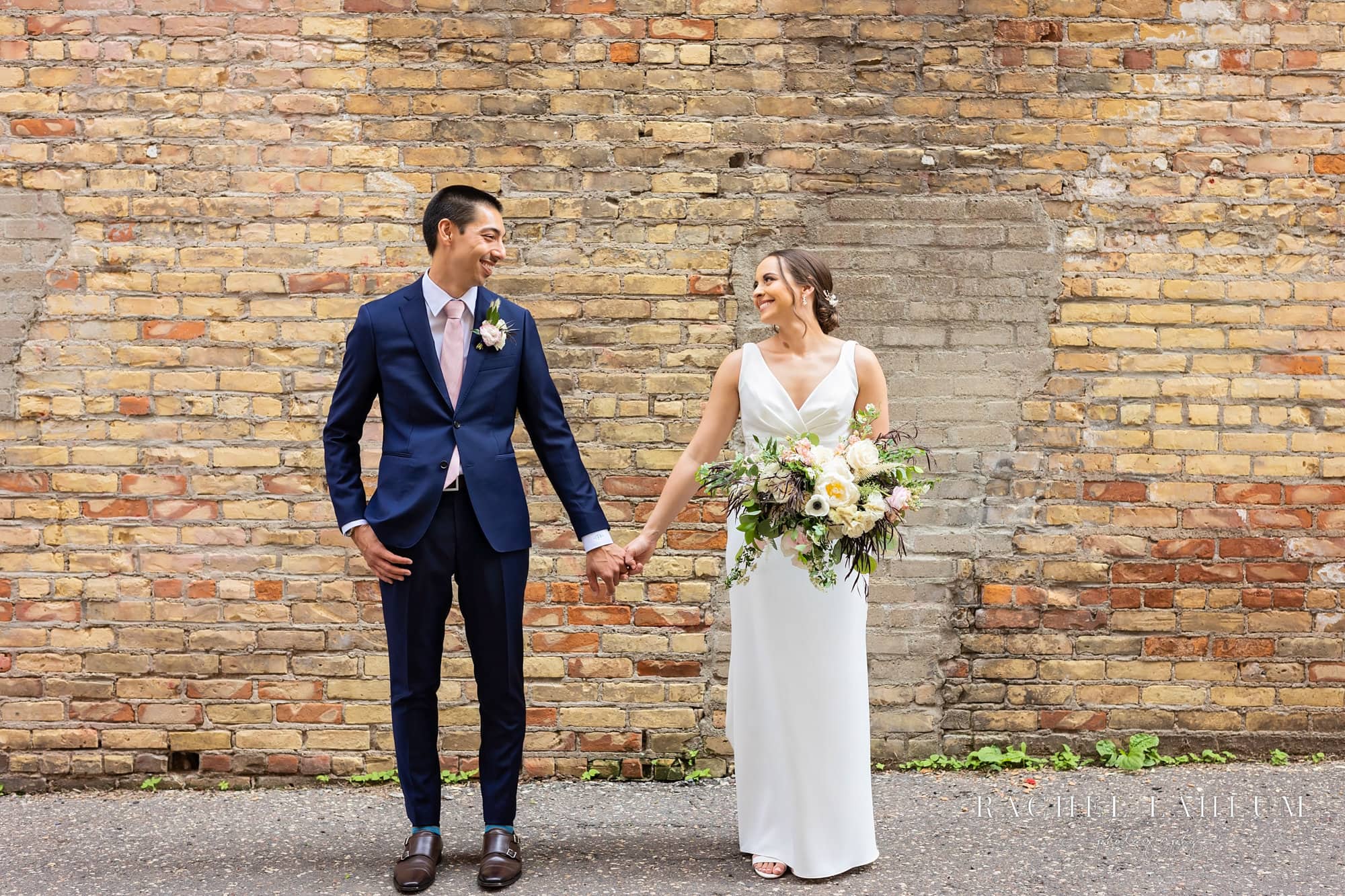 Newly wed couple hold hands and smile at each other in alleyway by Seventh Place Plaza in Saint Paul, Minnesota. 
