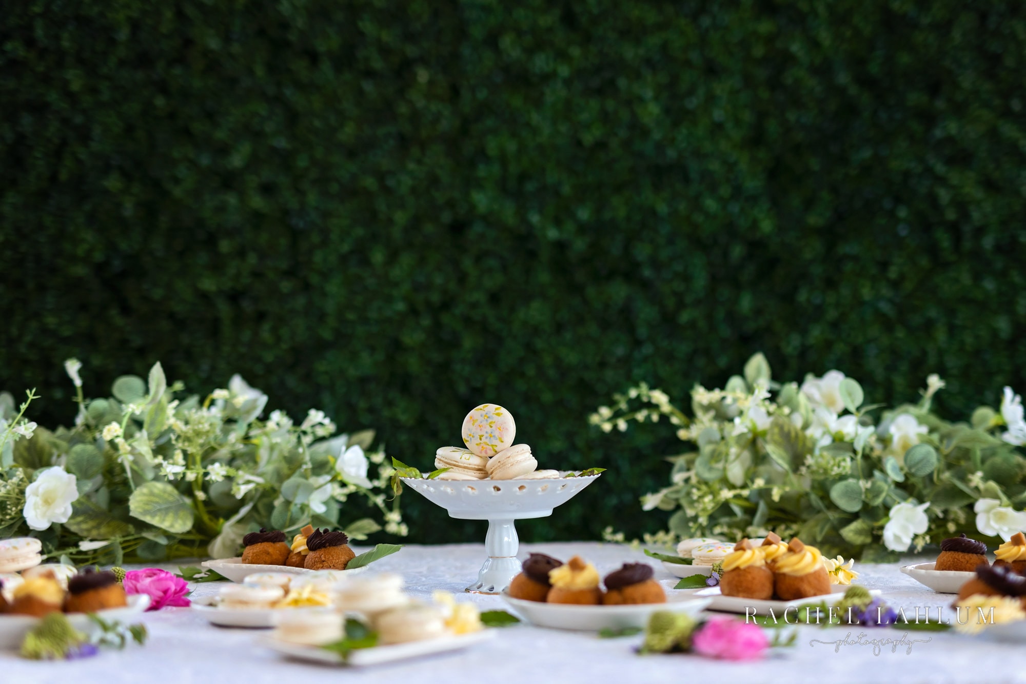 Desserts displayed in front of floral arrangements and live moss wall at Urban Daisy wedding space. 