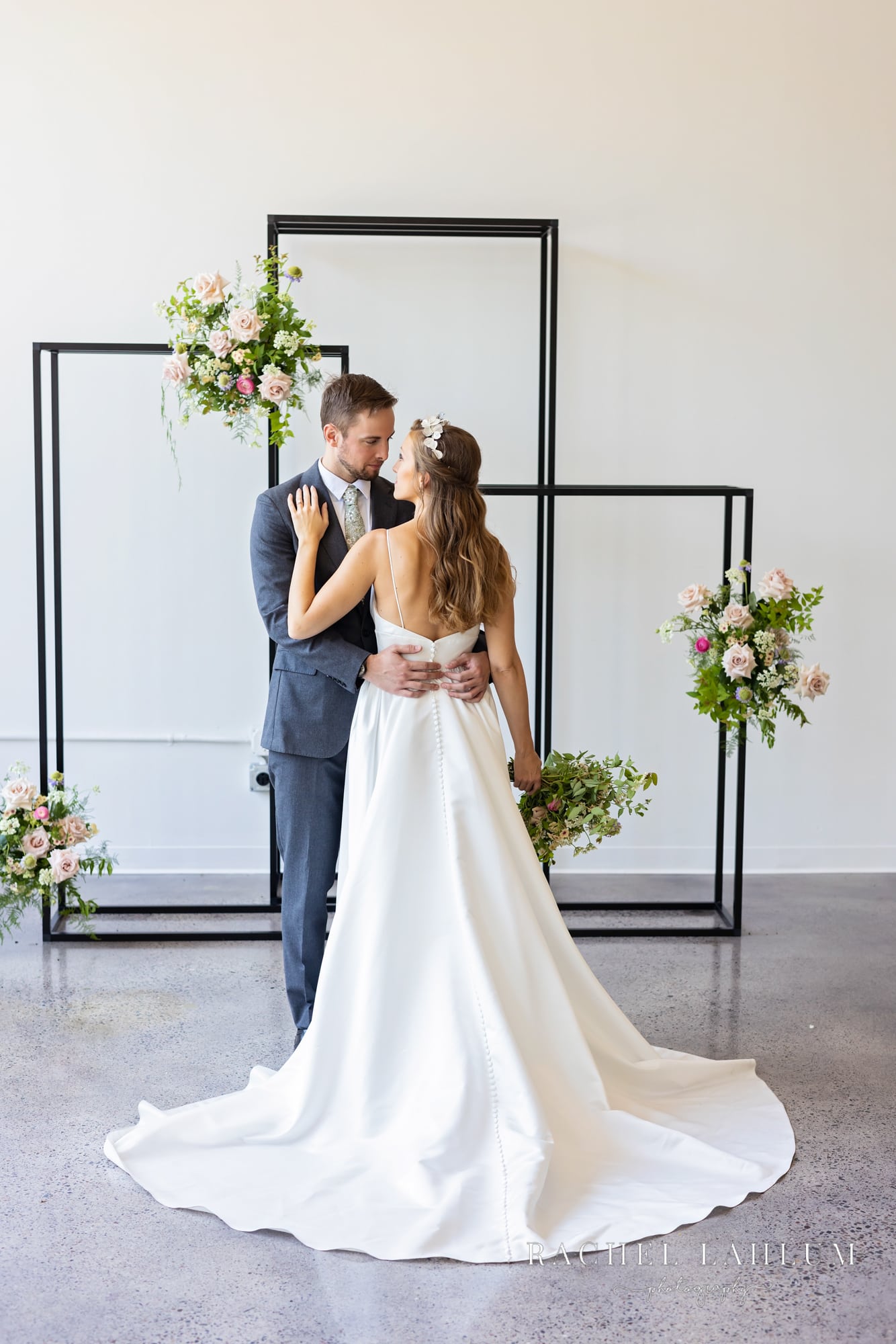 Bride faces groom in front of floral fixture during stylized shoot at Urgan Daisy. 