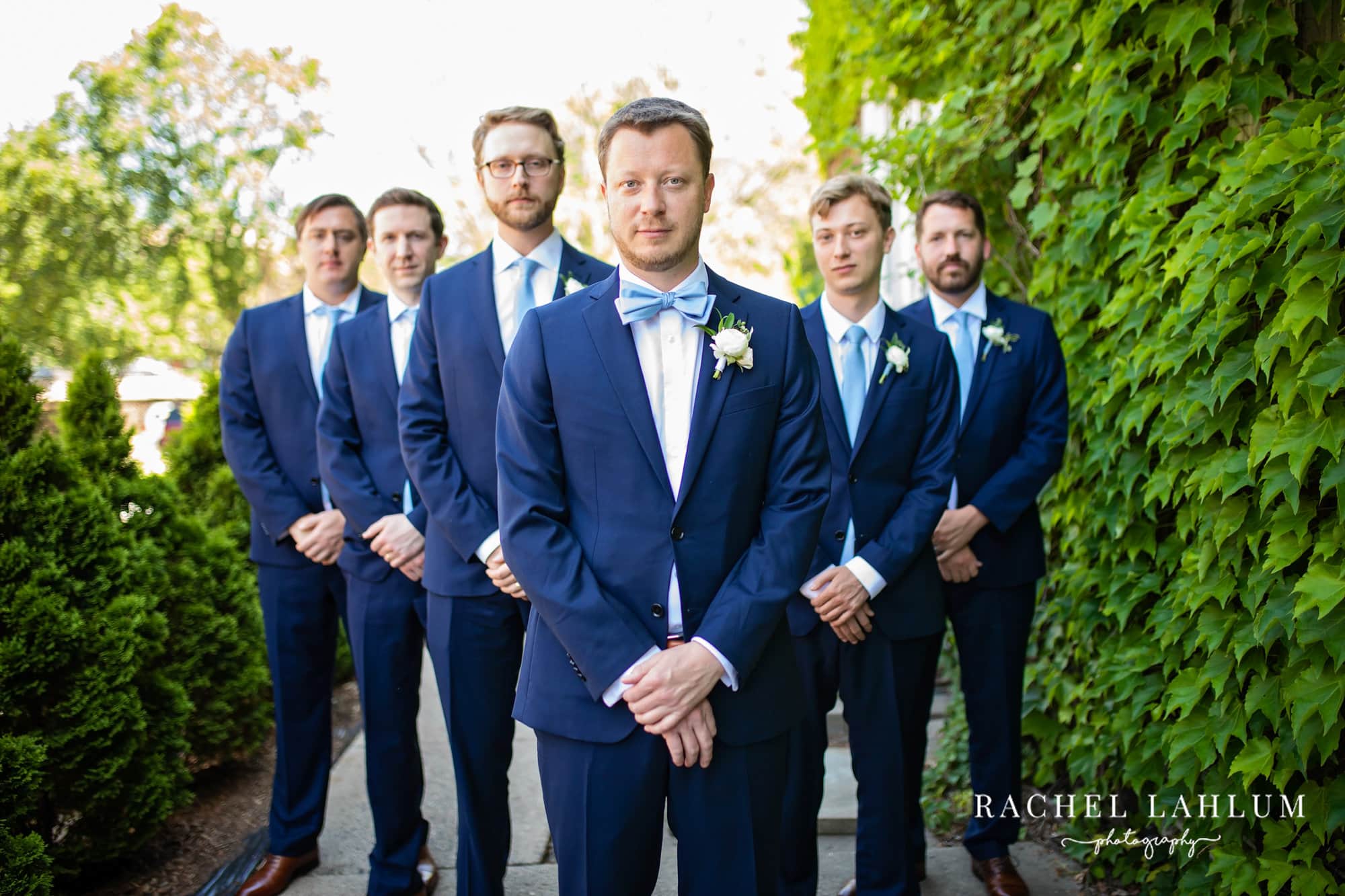 Groom and groomsmen pose in a v-shape in the garden at The Blaisdell Wedding Venue.