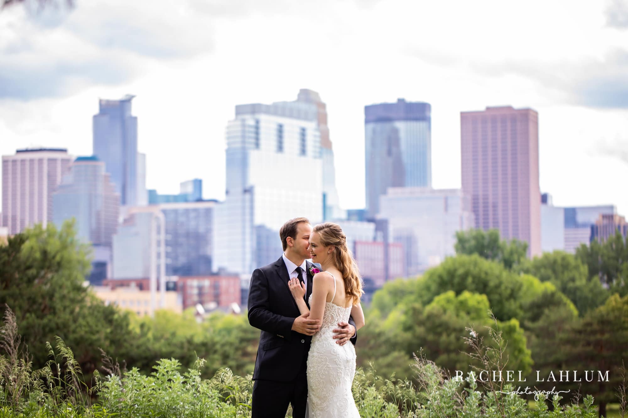 Groom kisses bride on the check in front of the Minneapolis skyline before wedding at Minneapolis Event Center. 