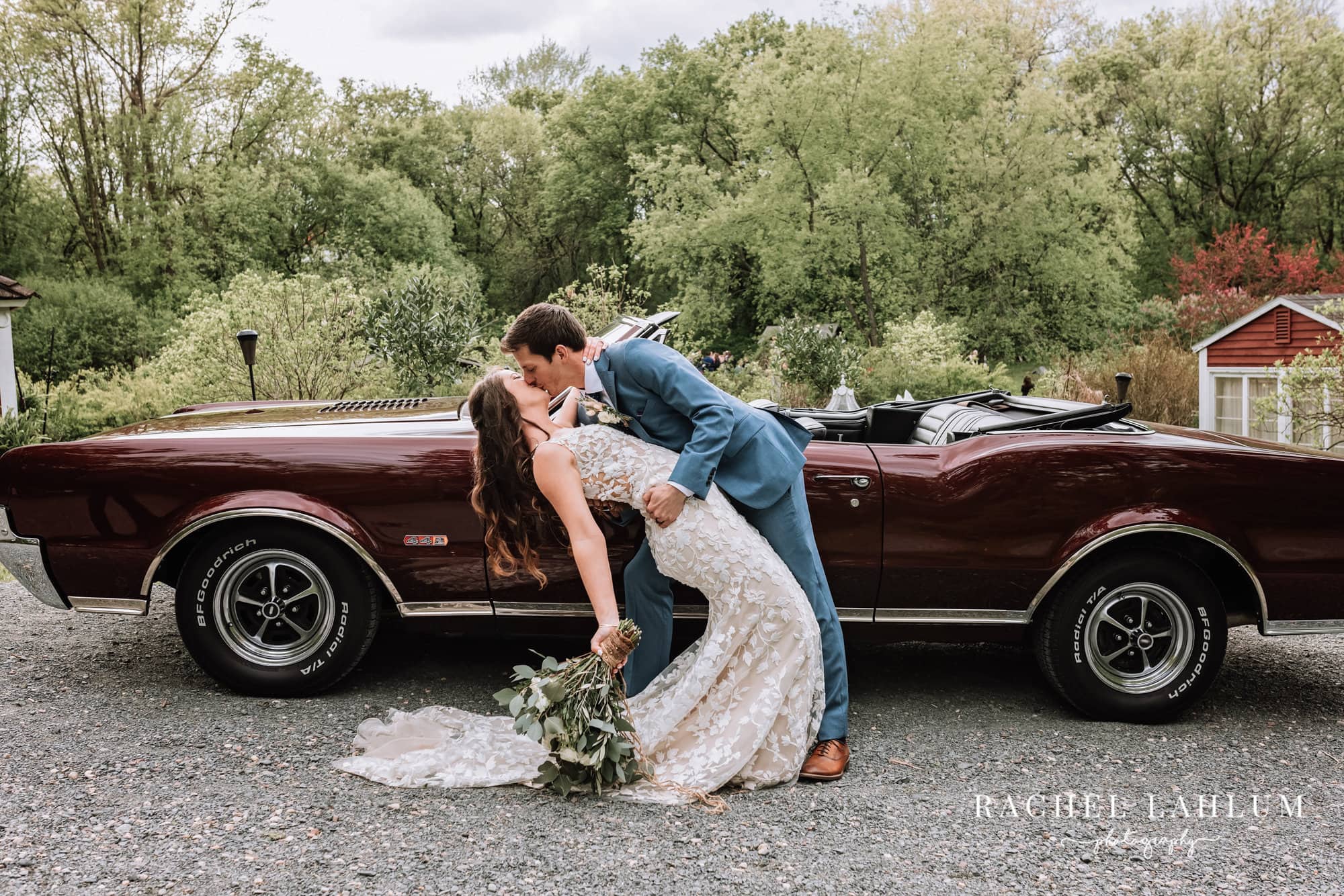 Groom dips bride and kisses here in front of classic car at Camrose Hill.