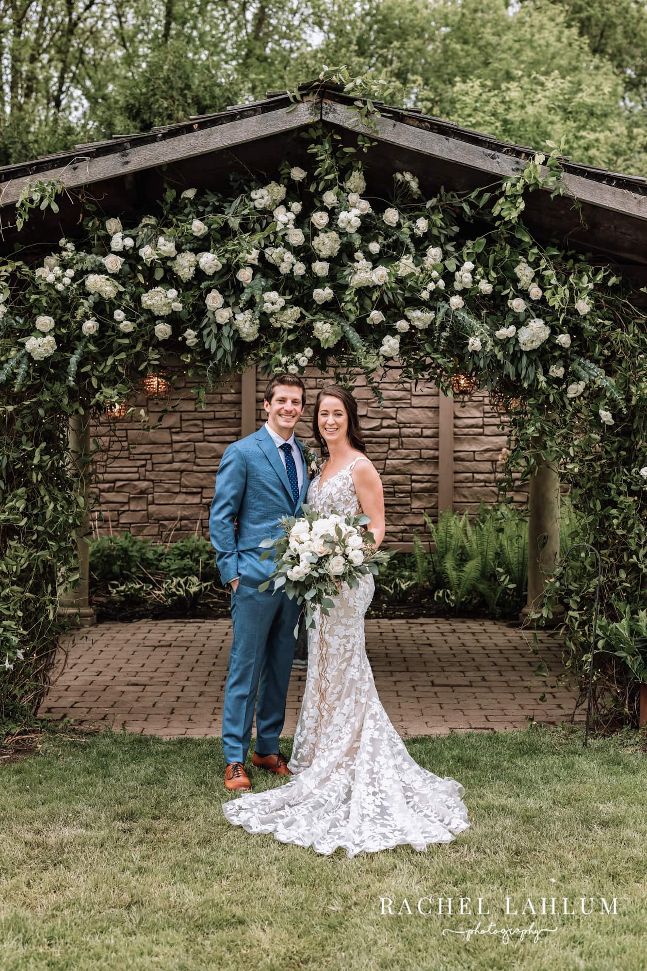 Newly wed couple pose under a floral archway before wedding at Camrose Hill Flower Farm in Stillwater, Minnesota.