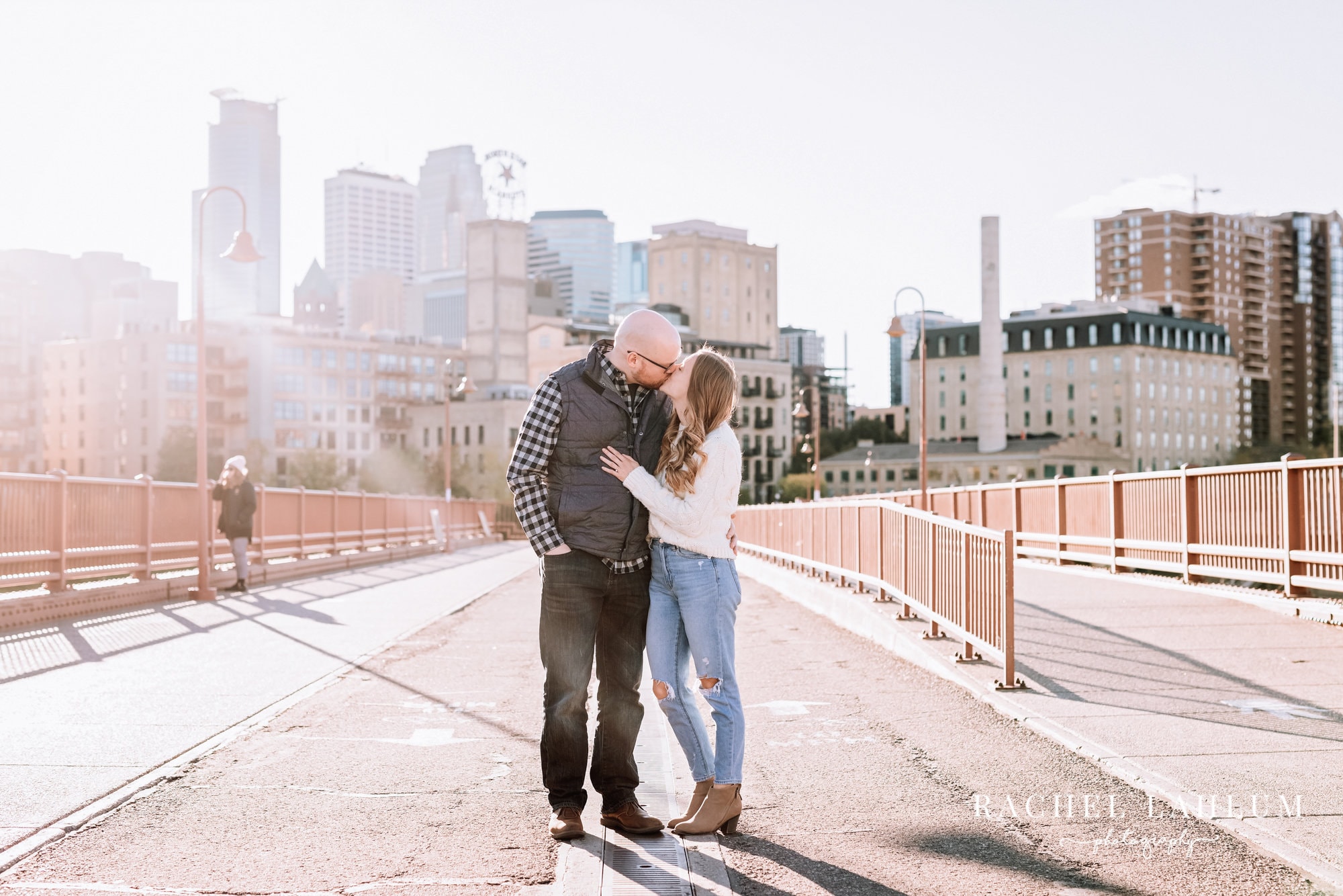 New engaged couple kiss on the Stone Arch Bridge with the Minneapolis Skyline behind them. 