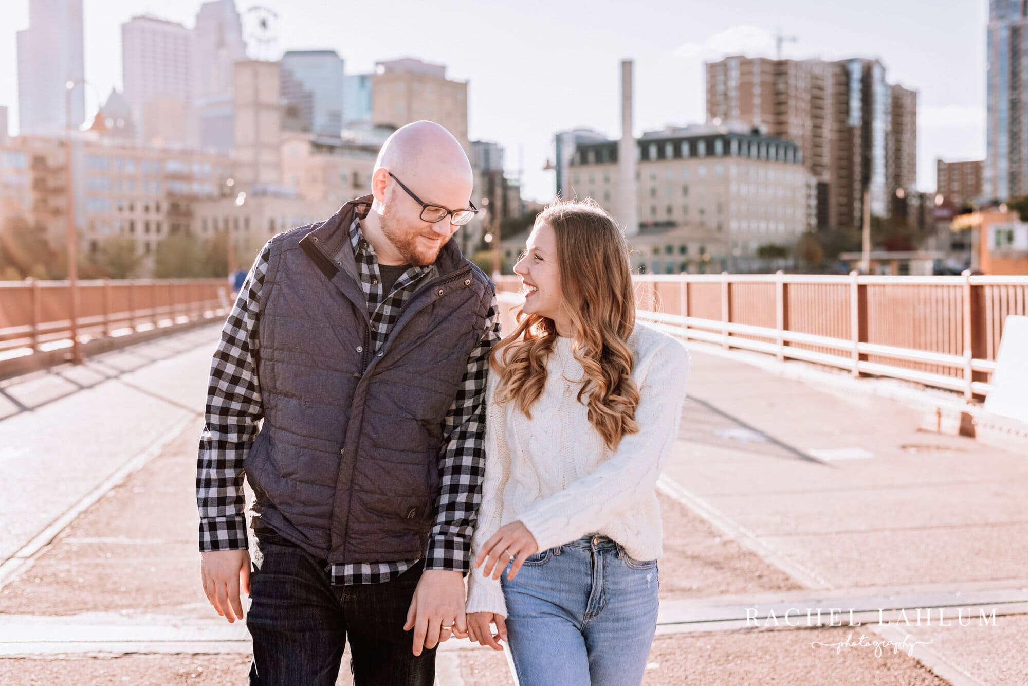 Engaged couple interlock pinkies and walk down the Stone Arch Bridge in Minneapolis.