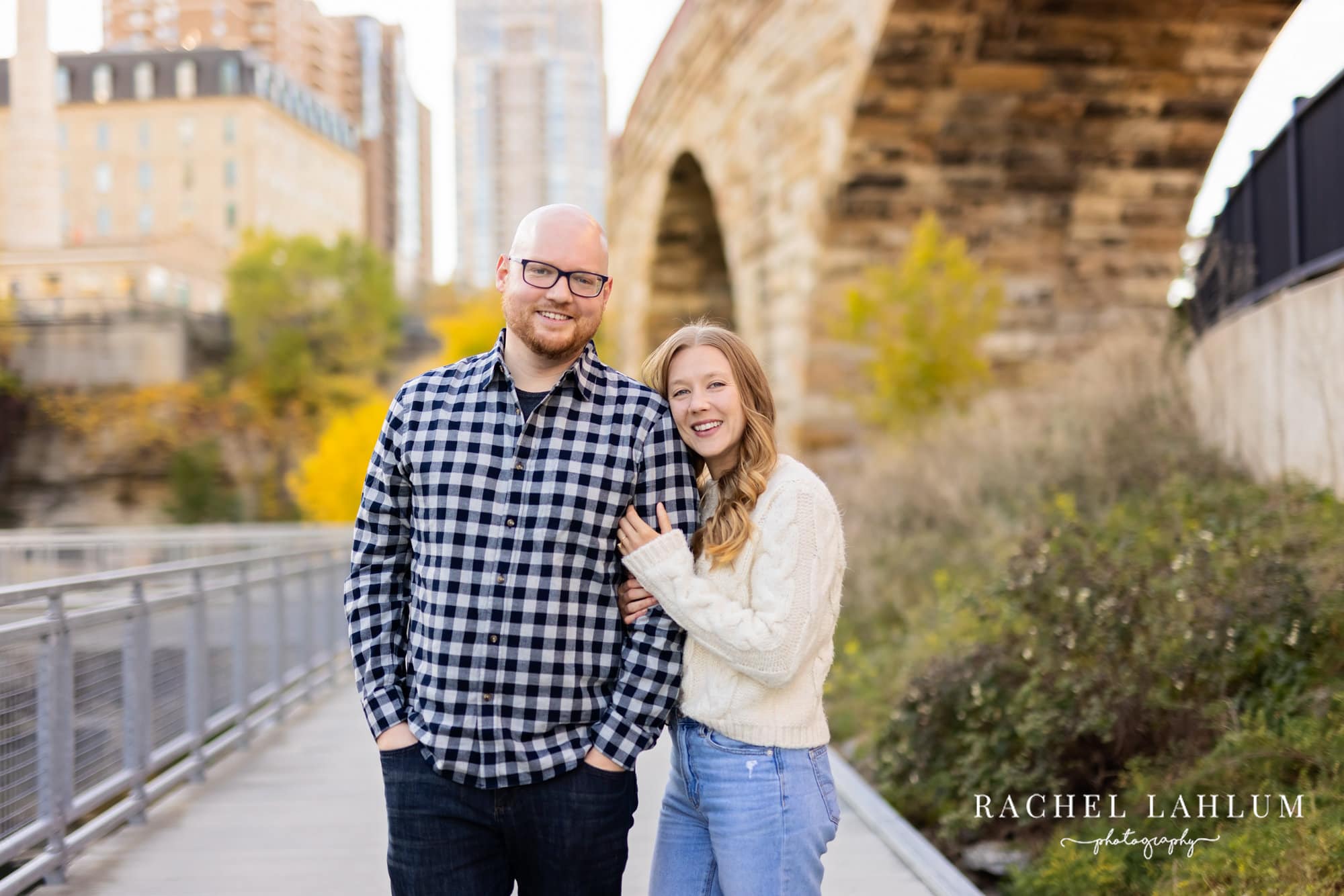 Newly engaged couple pose under the Minneapolis Stone Arch Bridge.