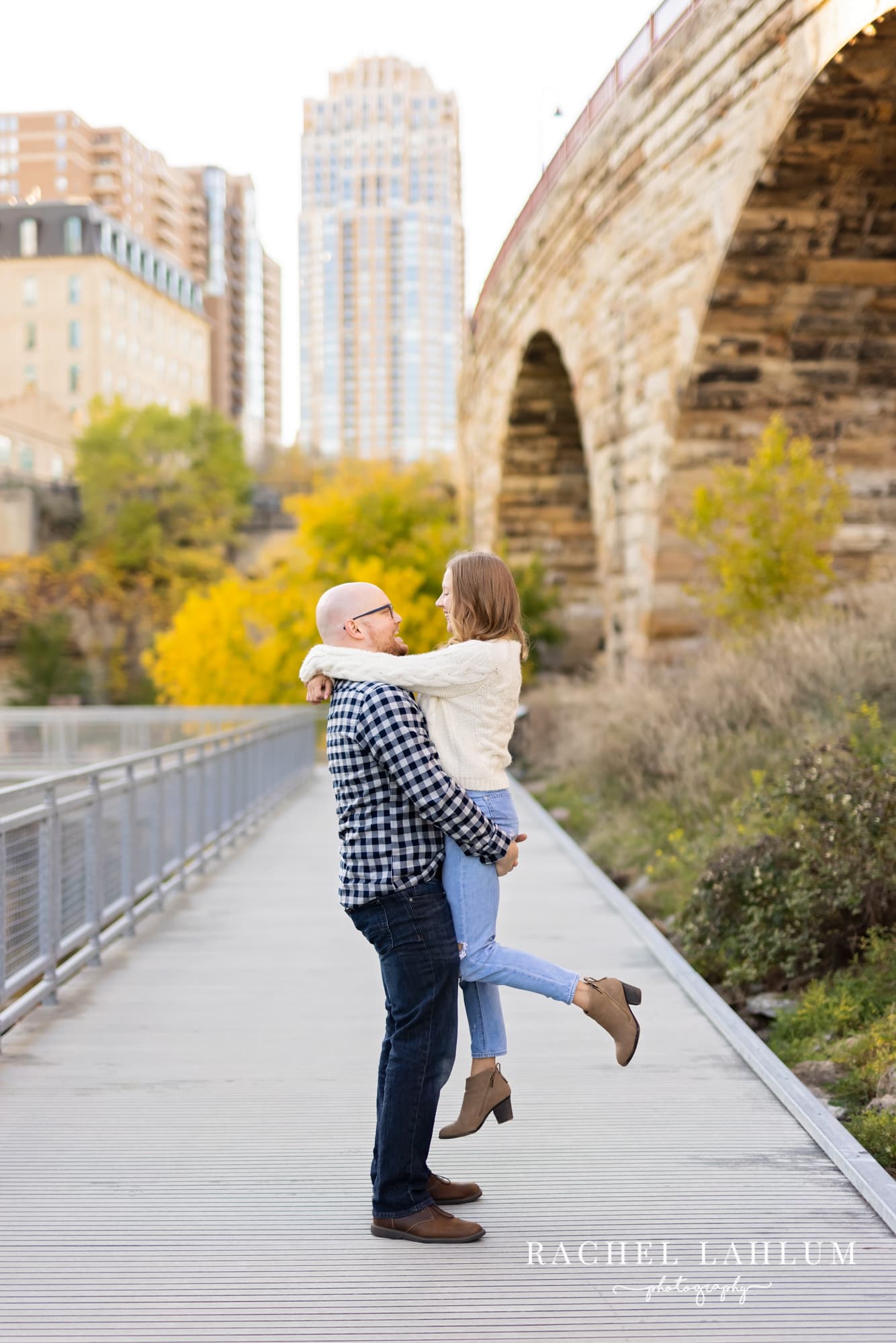 Man picks up women during engagement photo session under the Stone Arch Bridge.