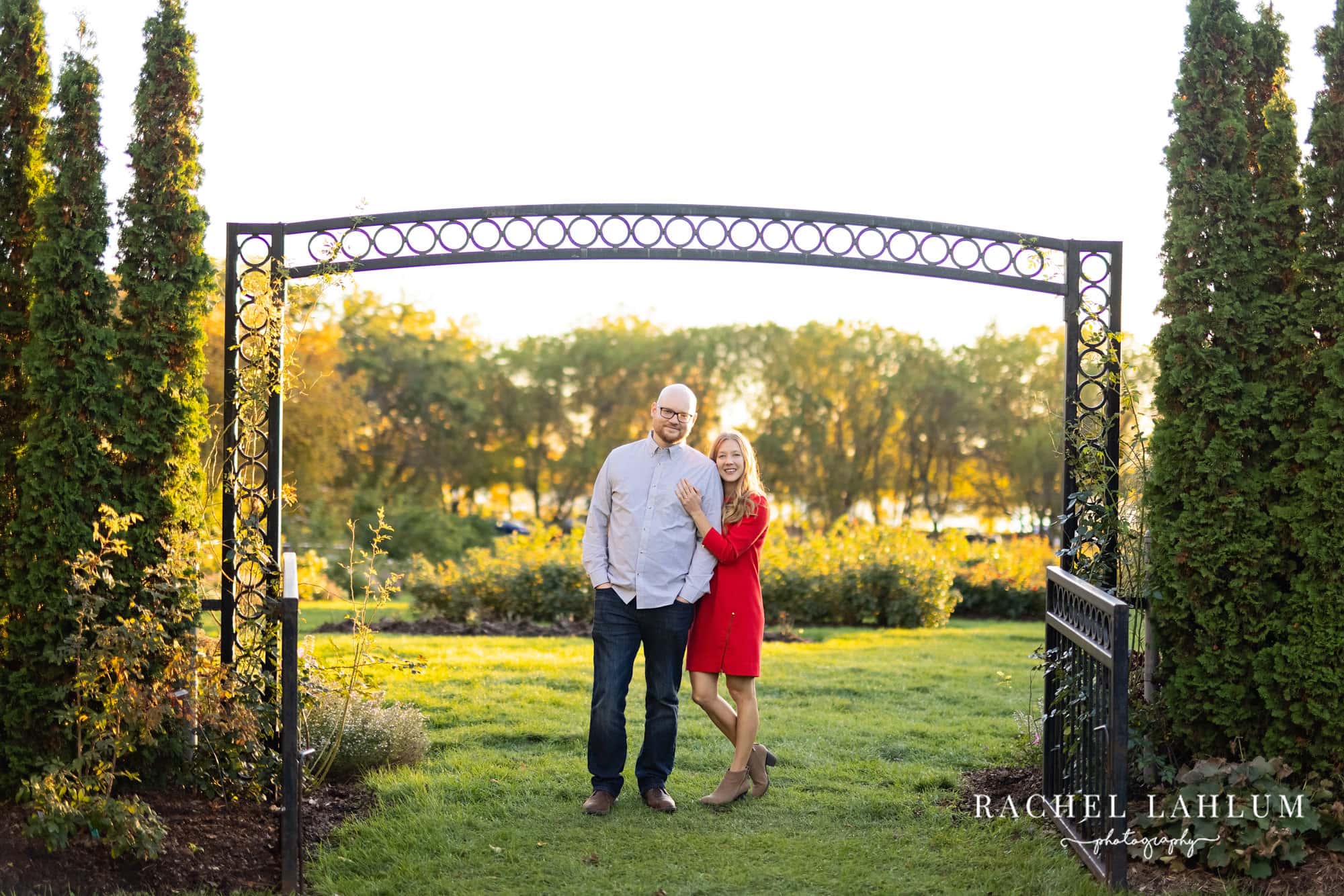 Newly engaged couple pose under a wrought iron archway at Lyndale Rose Gardens.