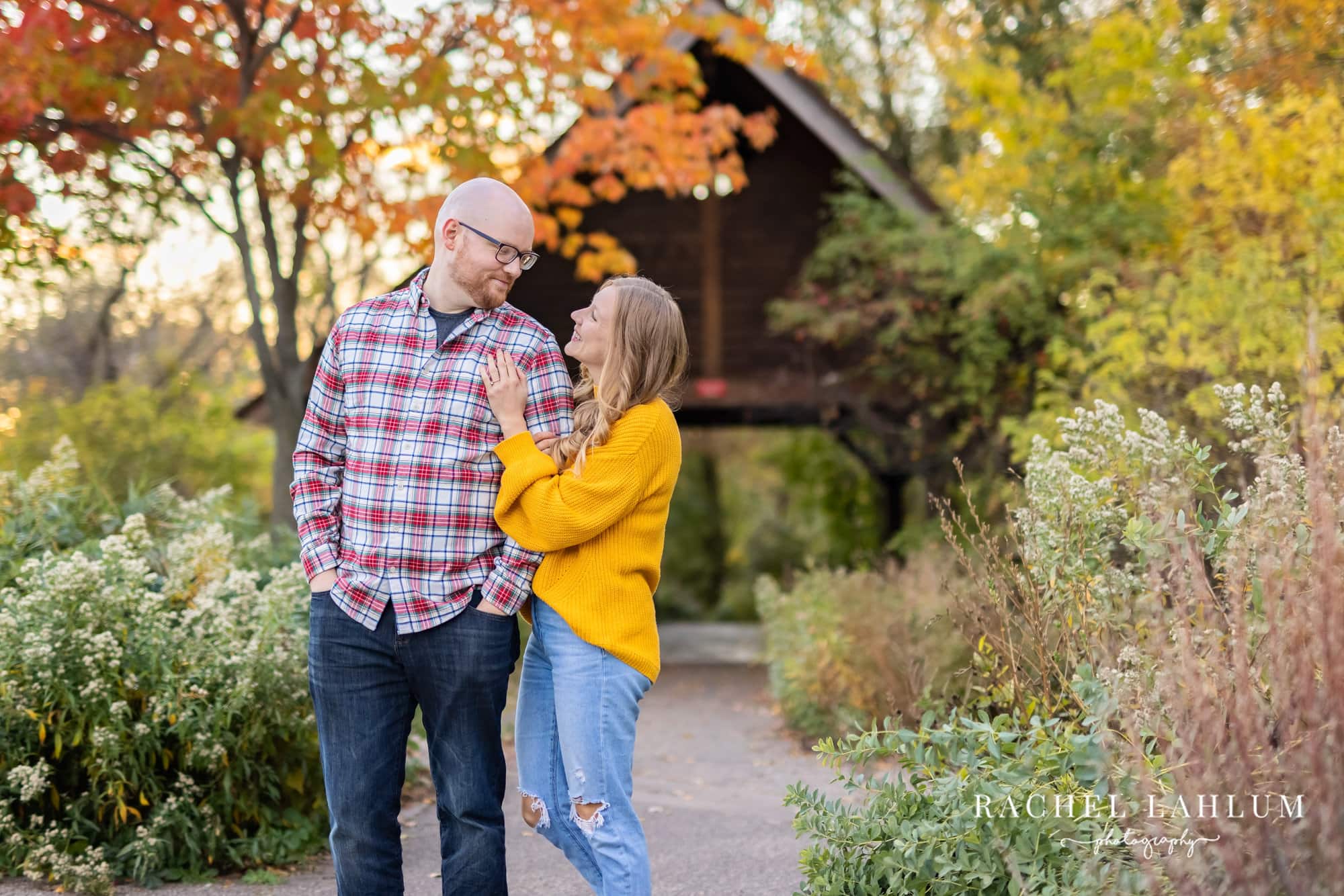 Newly engaged couple look into each other’s eyes in front of a covered bridge at Lyndale Rose Gardens.
