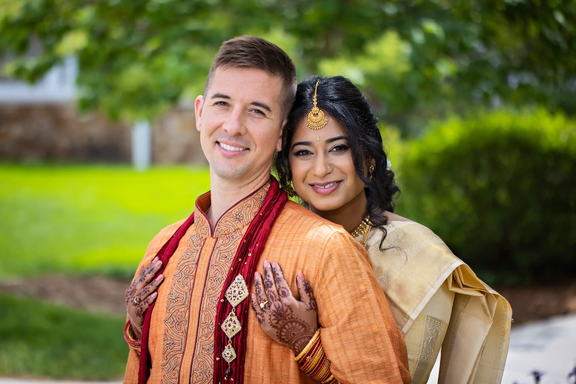 Bride and groom wearing traditional orange and yellow Indian wedding attire pose for their wedding photography at Glenn Oaks Country Club in Des Monies, IA.