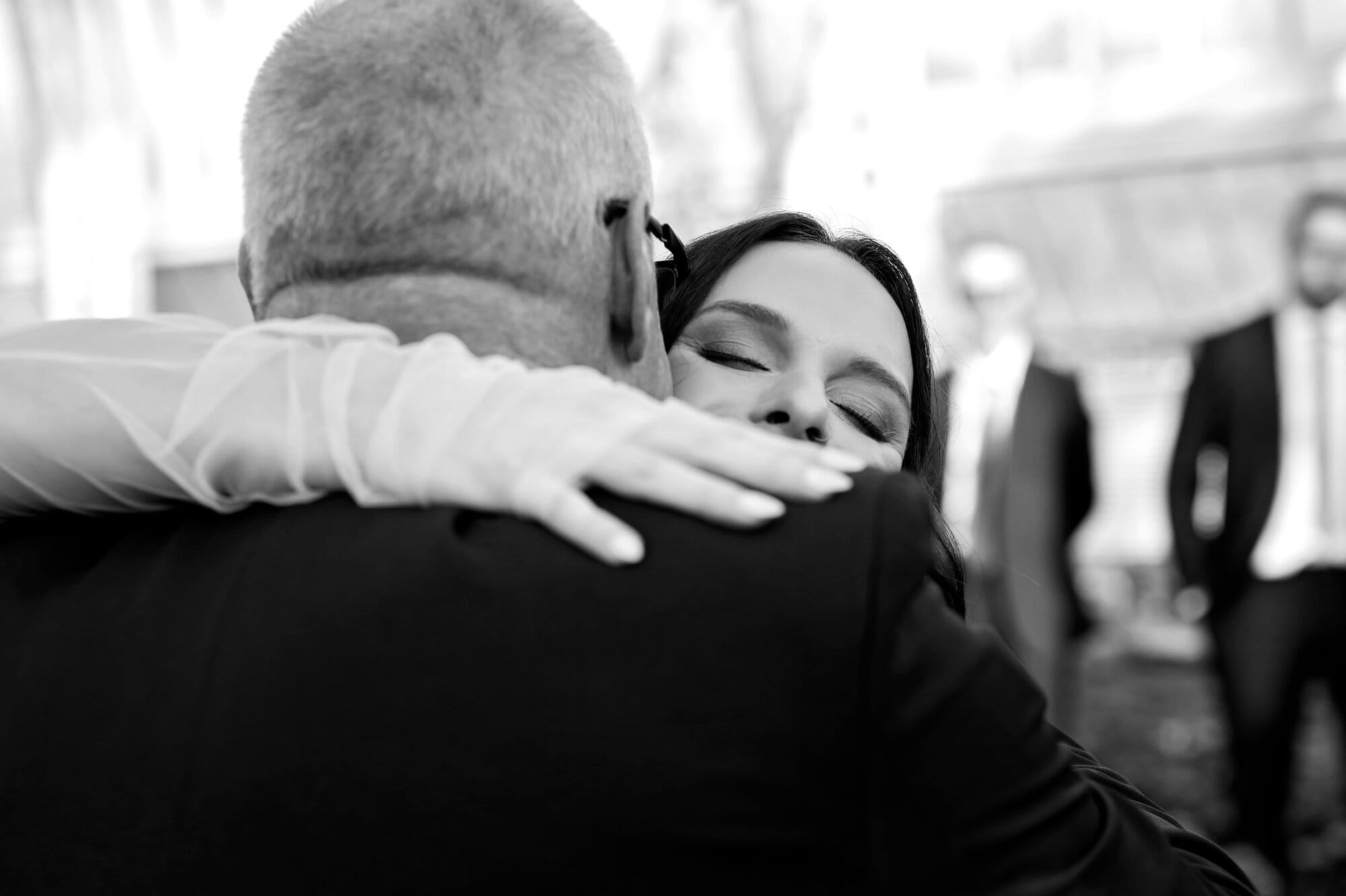 A black and white candid wedding photo of a bride hugging her dad during her wedding ceremony at the Como Conservatory Sunken Garden in St. Paul, MN.