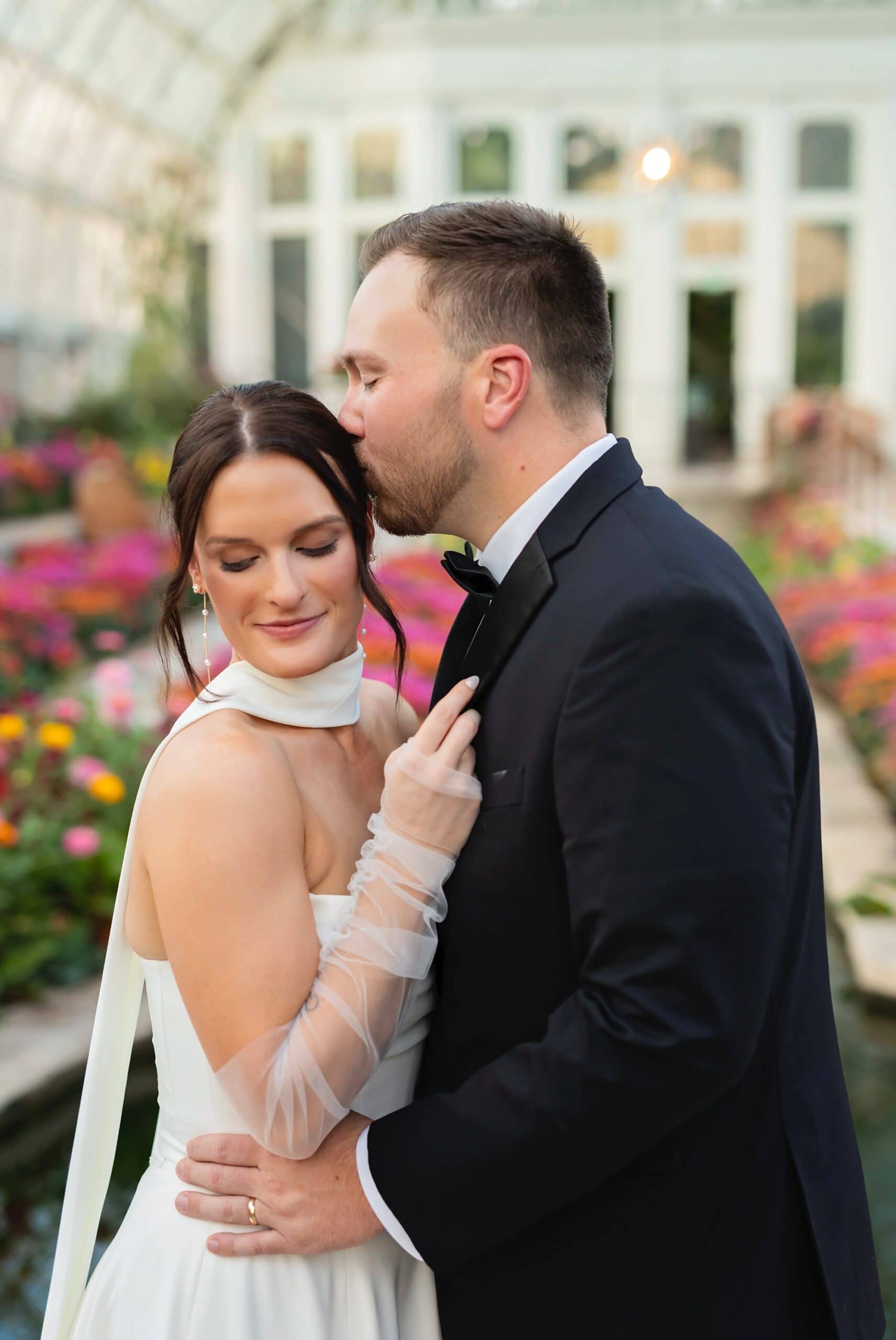 A groom kisses a bride on the side of her head for their wedding photos in Como Conservatory Sunken Garden.