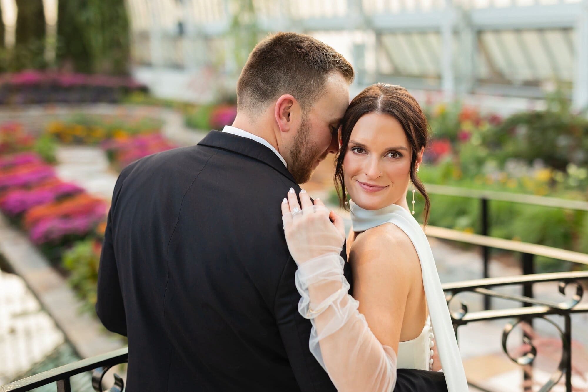 A bride and groom pose for their romantic micro wedding photography at Como Conservatory in St. Paul, MN. The bride has her arm wrapped around the groom's shoulder and is smiling at the camera while the groom rests his forehead along her temple.