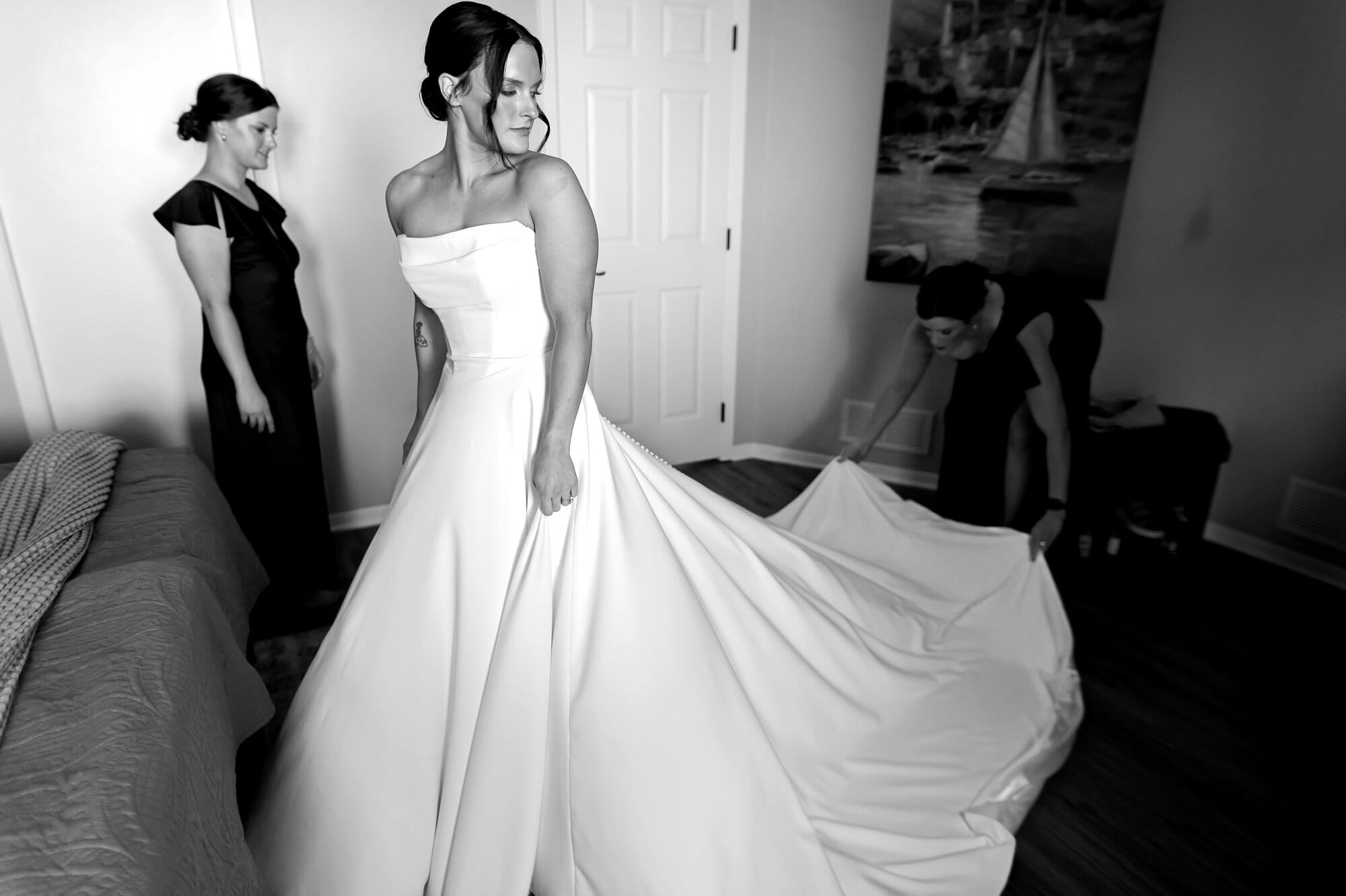 A bride looks over her shoulder as her sister fluffs the train of her wedding dress in her micro wedding photography.