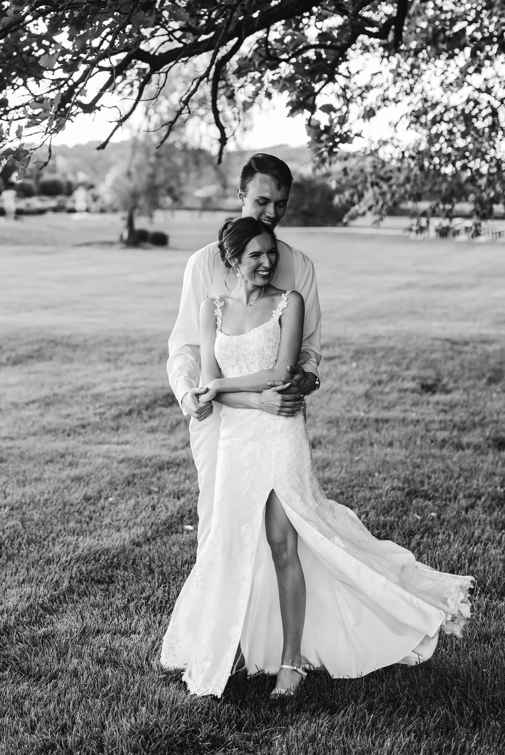 Bride laughing as the groom wraps his arms around her during romantic outdoor wedding portraits at Ridgetop Events in Prescott, Wisconsin.