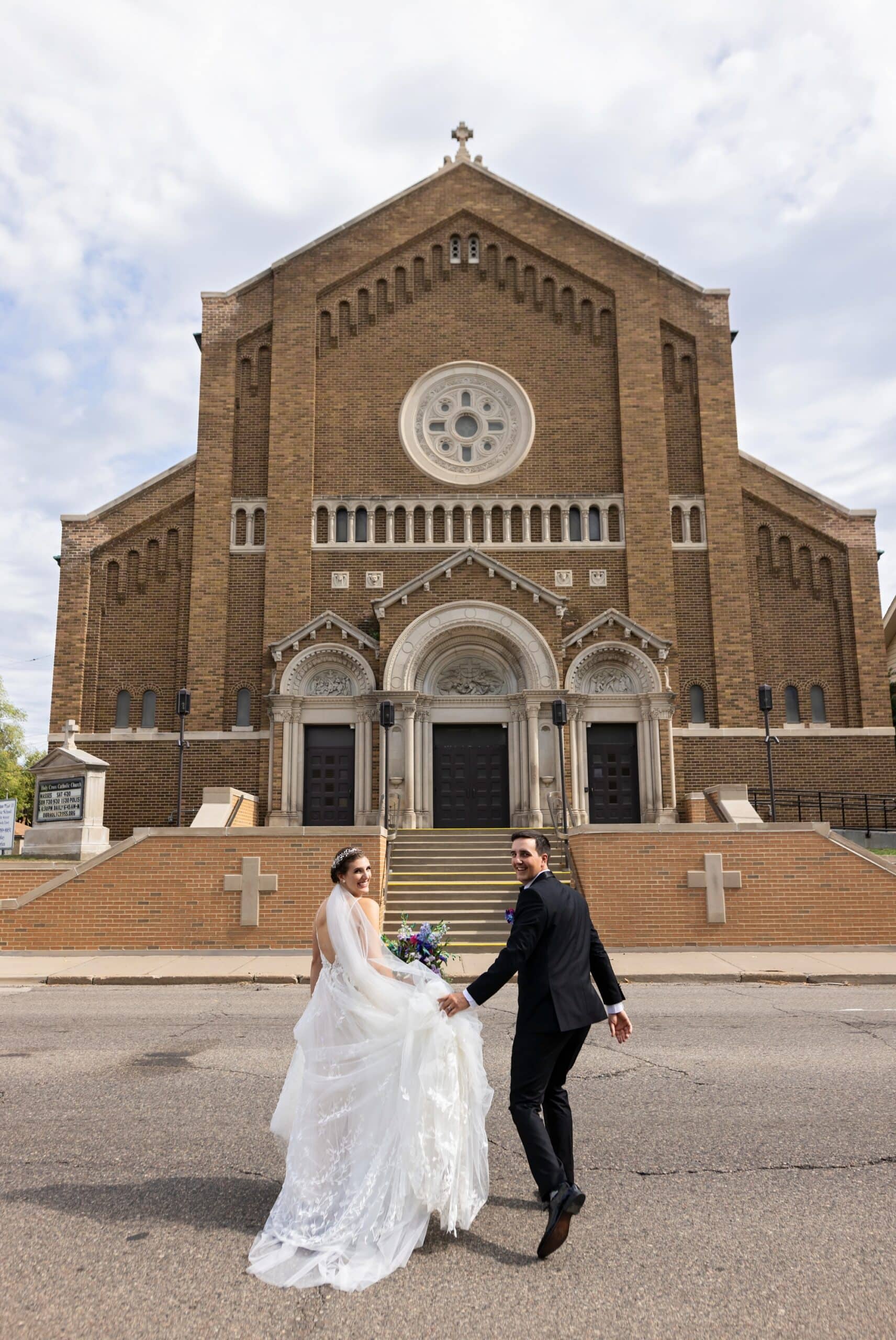 Stunning view of bride and groom posing hand in hand in front of the Holy Cross Catholic Church, NE Minneapolis