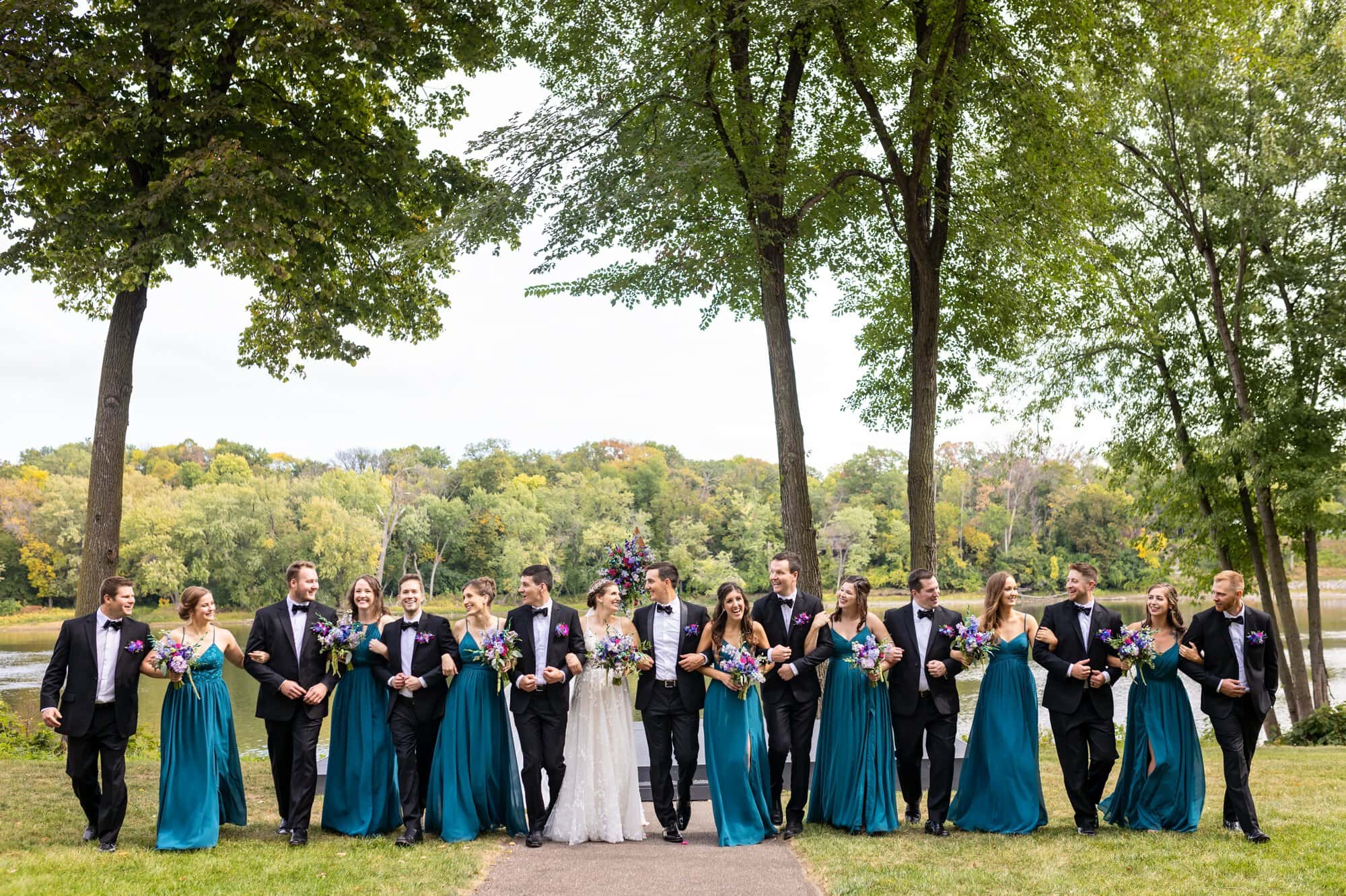 Wedding party linking arms for a group portrait walking through Leopold's Mississippi Gardens, NE Minneapolis