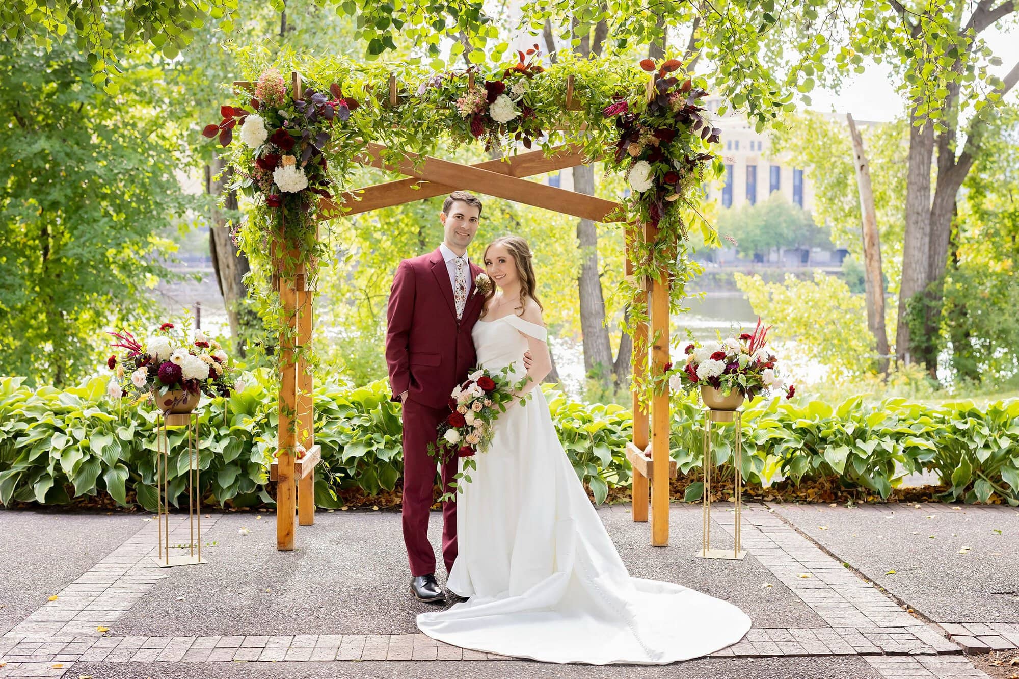 A bride and groom pose together under a wedding arch for a wedding photography portrait at the Nicollet Island Pavilion wedding