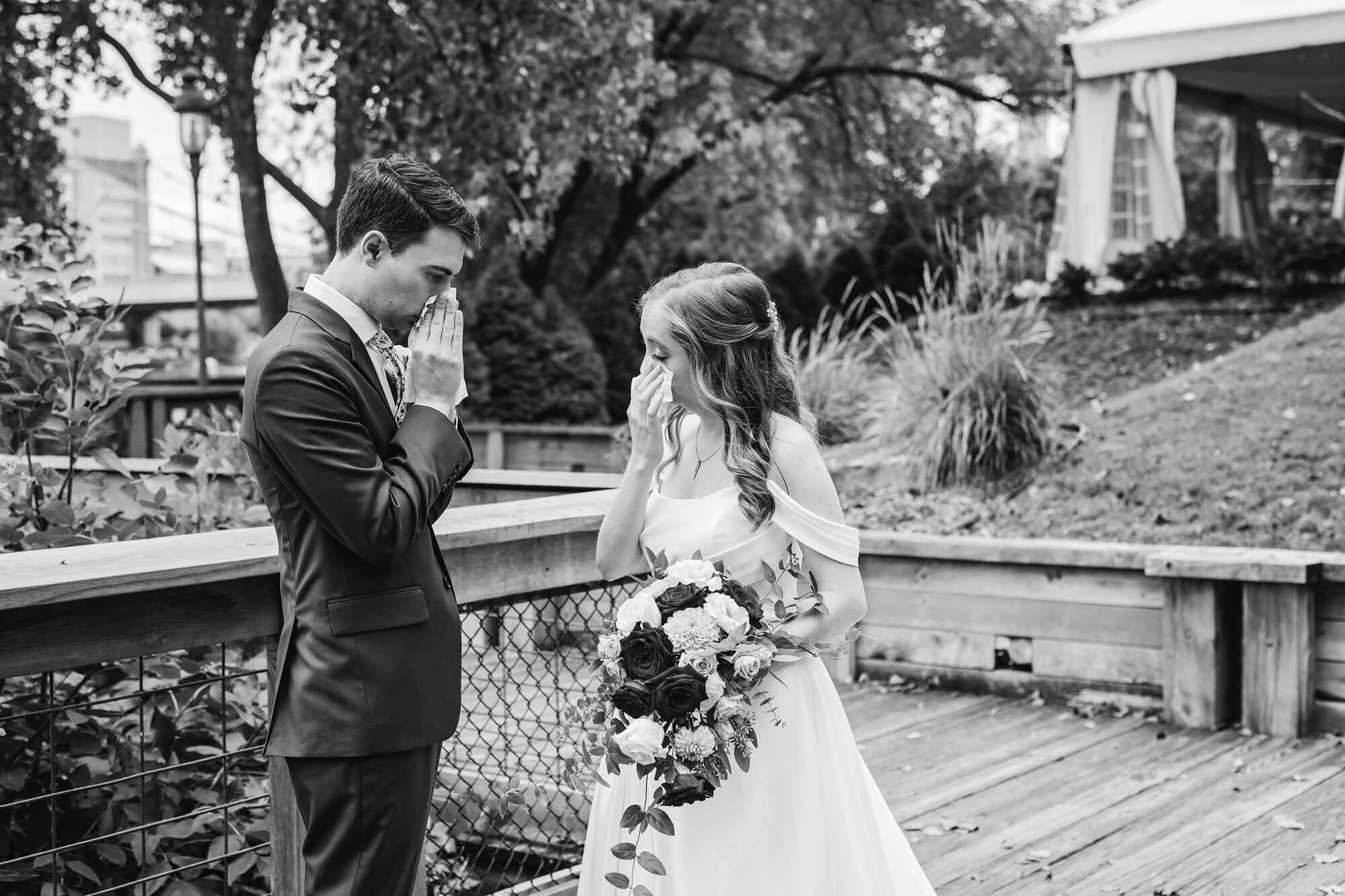 Bride and groom wipe tears from their faces in an emotional moment after their first look on the Nicollet Island boardwalk in Minneapolis, MN