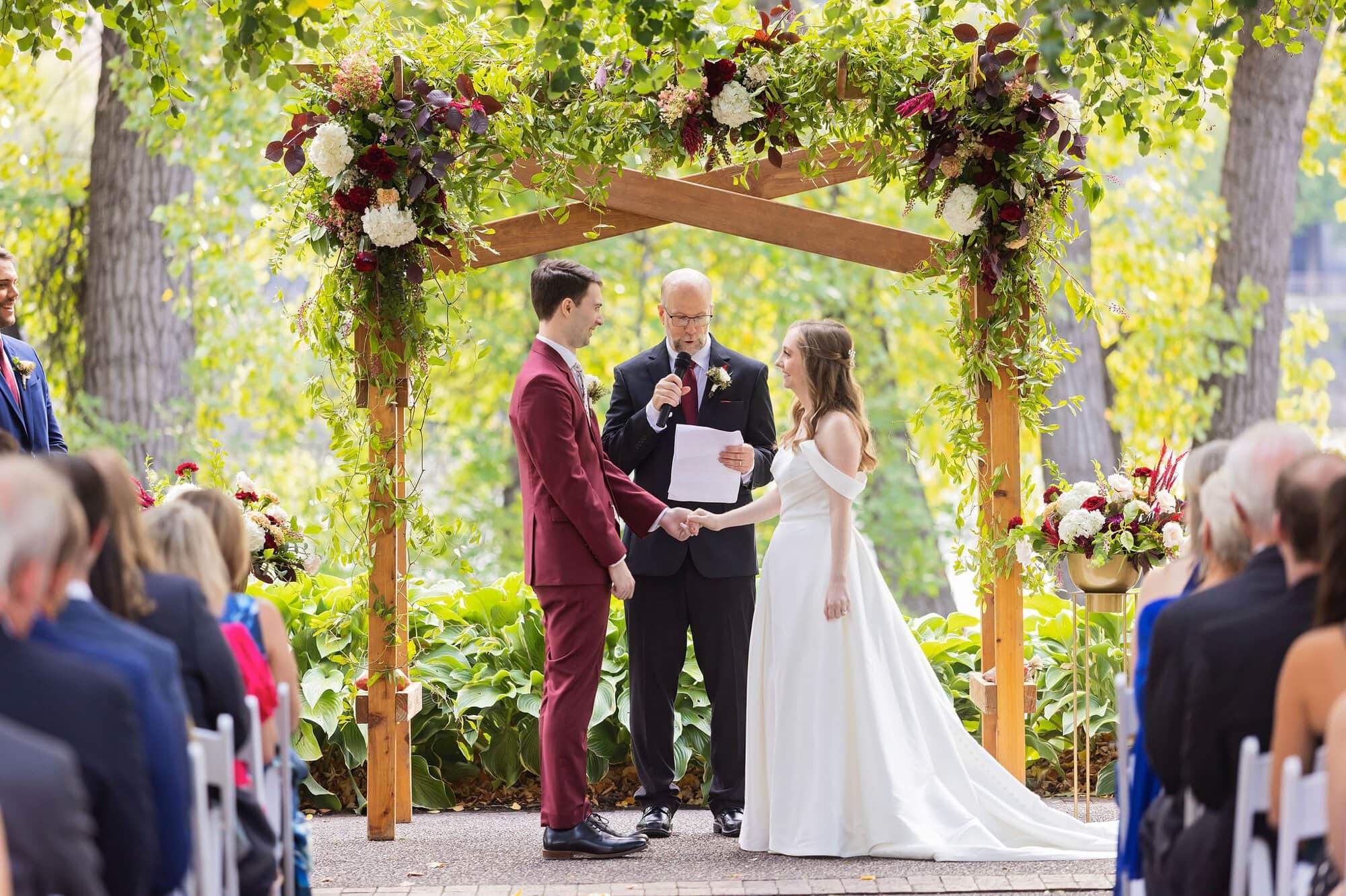Bride and groom hold hands in front of the officiant at a wedding on the Nicollet Island Pavilion patio in Minneapolis Minnesota