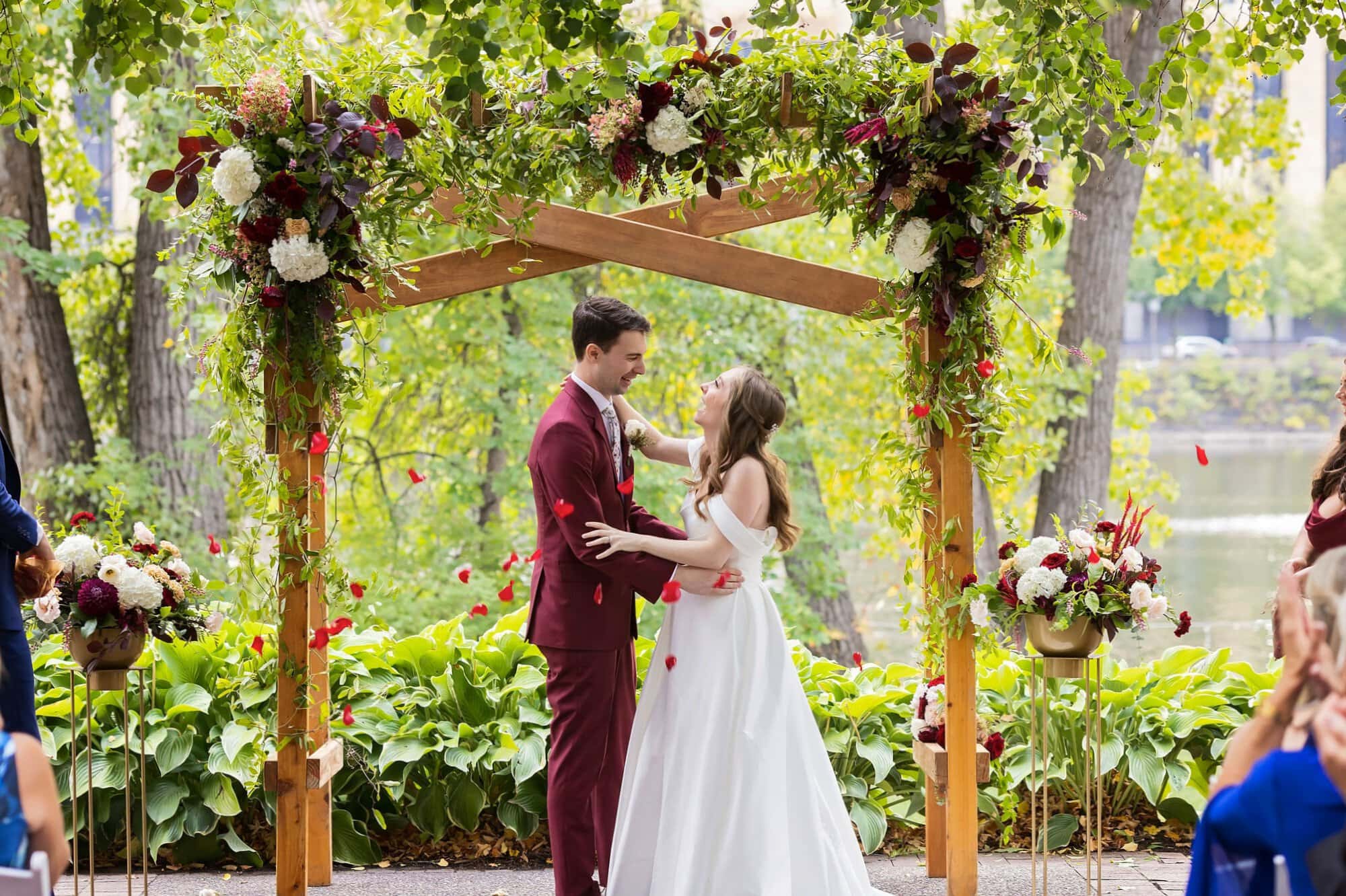 Bride and groom laugh while standing under a wedding arch at the wedding reception on the Nicollet Island Pavilion patio in Minneapolis Minnesota