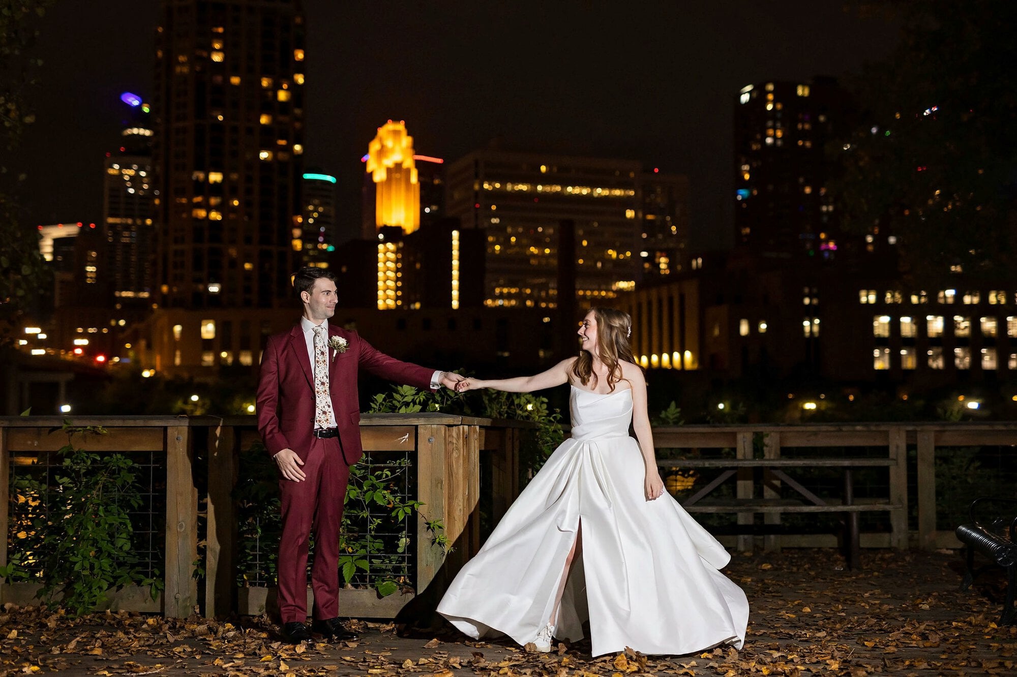 Bride and groom dancing before a night time skyline for sunset portraits at the Nicollet Island boardwalk in Minneapolis Minnesota