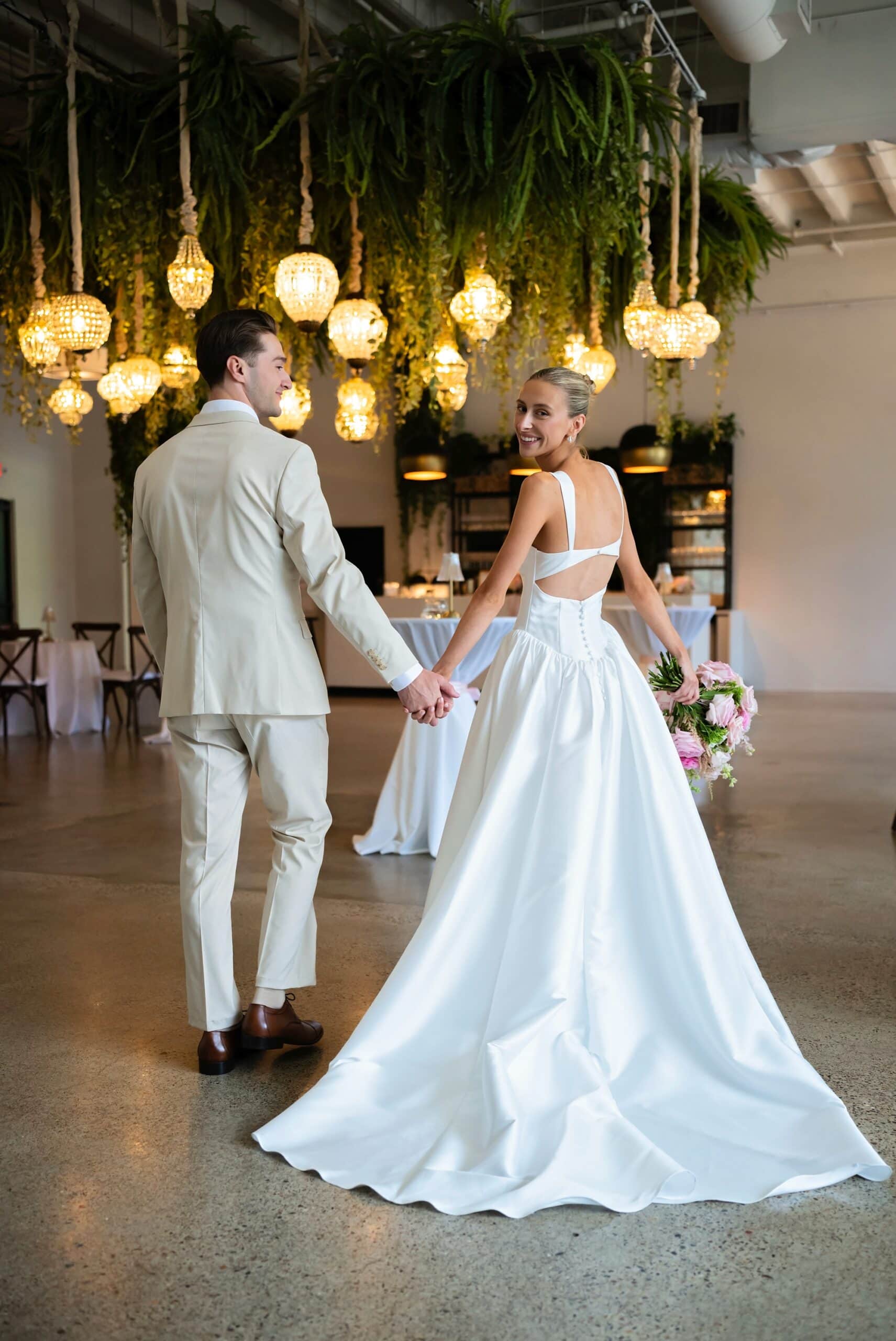 Bride and groom hold hands and look over their shoulders at the camera for couple photos at Urban Daisy wedding venue in Minneapolis, Minnesota