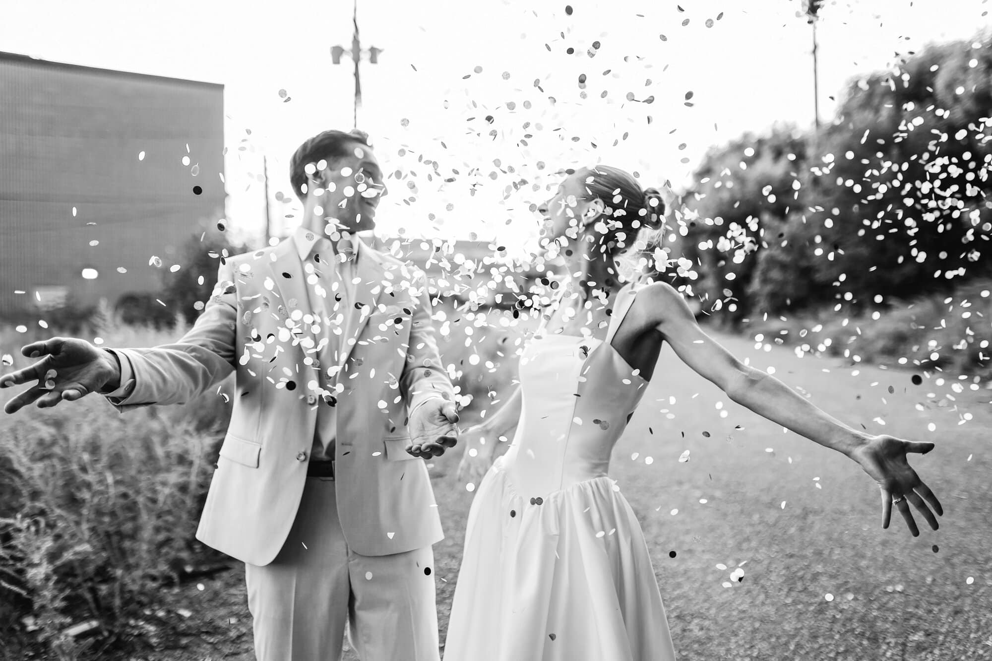 Bride and groom laugh as confetti falls on them in a black and white post-ceremony photo at a relaxed Urban Daisy wedding in Minneapolis, Minnesota